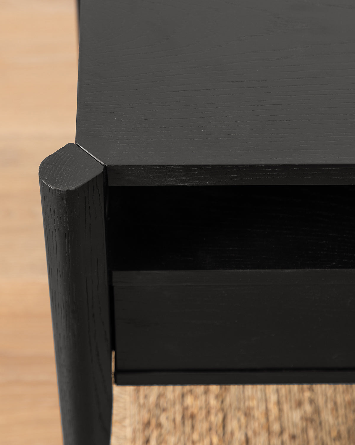 Close-up of the Dana Nightstand’s black wood corner, showing its shelf and drawer on a wooden floor, by McGee & Co.