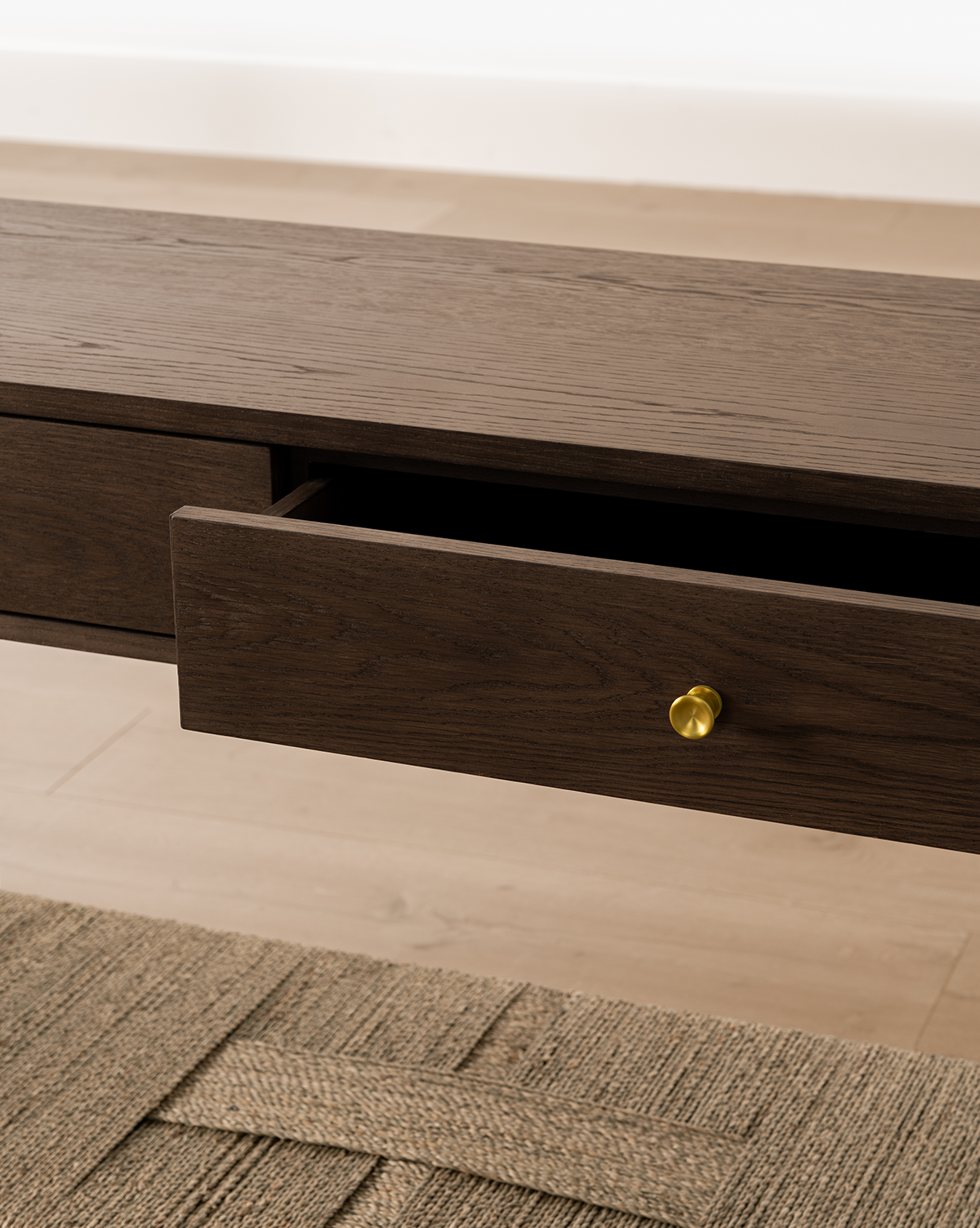 A close-up of the Dana Walnut Oak Console with an open drawer and brass knob, set on a light wood floor beside a textured beige rug, by McGee & Co.
