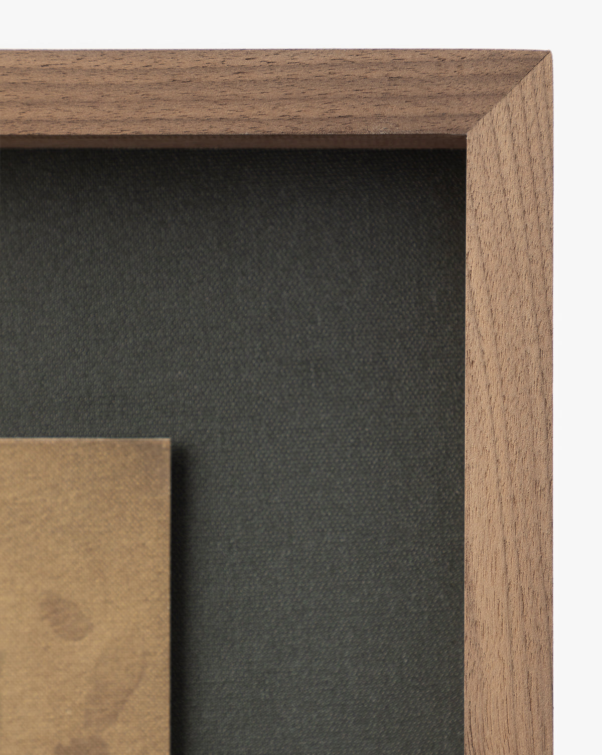 Close-up of the top right corner of the rustic walnut Dappled frame, shown against a dark fabric background with a beige mat or artwork featuring deckled edges visible in the lower left, by McGee & Co.