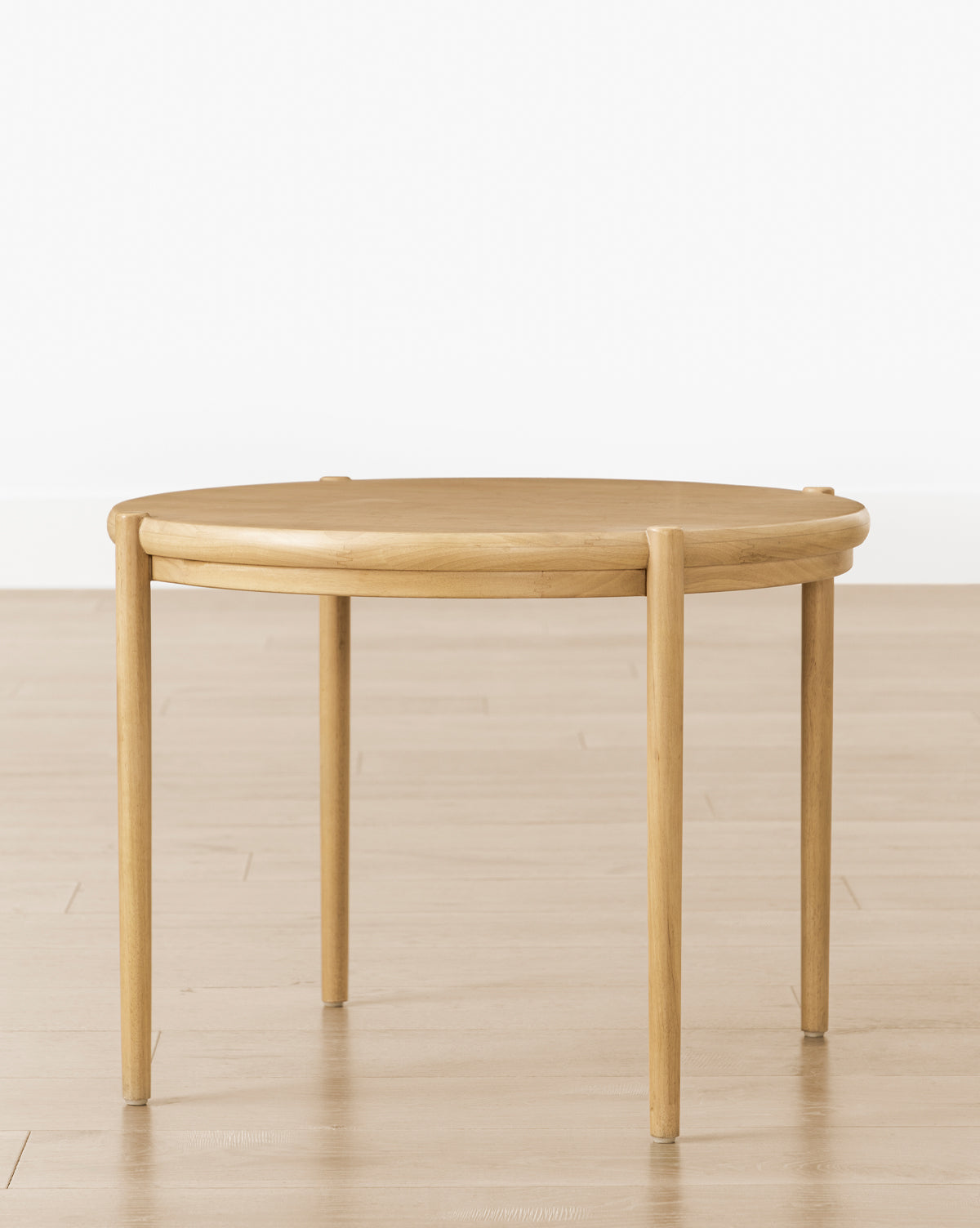 The Darcy Kids Table, a round, light white oak table with four straight legs, sits on a light wooden floor against a plain white wall—perfect as a stylish crafts or kids table for creative spaces, by McGee & Co.