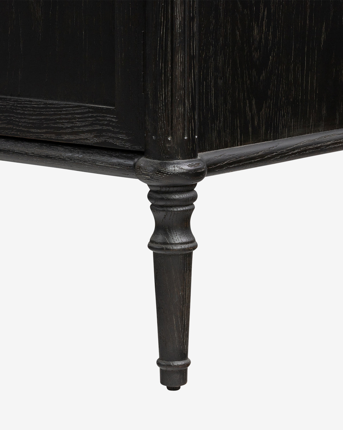Close-up of the Dixon Sideboard’s dark wooden leg, featuring ornate detailing and a turned, tapered design against a plain white background; complements the sideboards aged brass hardware, by McGee & Co.
