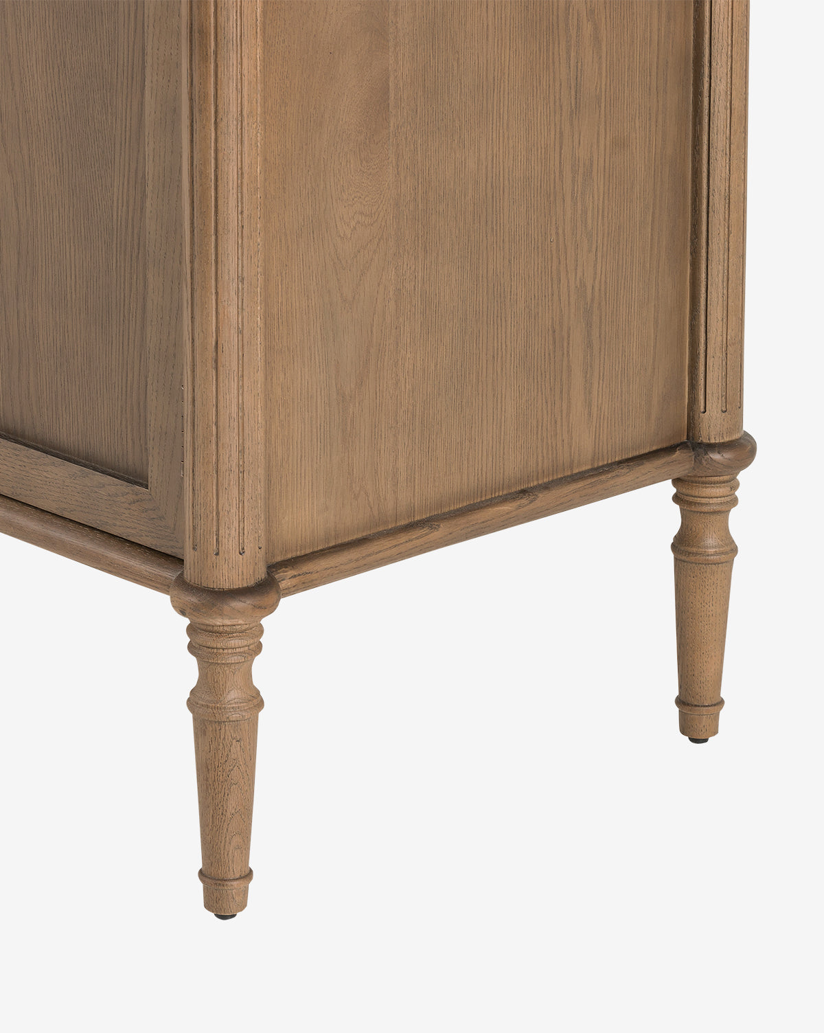 A close-up of the Dixon Sideboard’s lower corner shows its light brown finish, turned tapered legs, and subtle aged brass hardware, all set against a white background by McGee & Co.