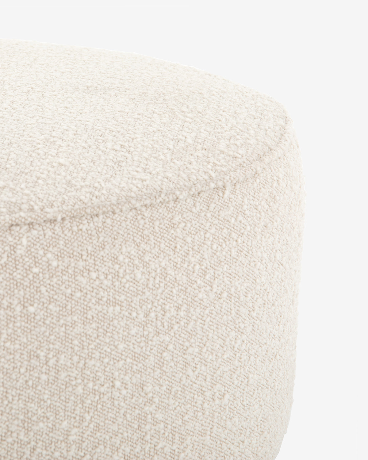Close-up of the top and side of the round, textured Dawson Ottoman in off-white upholstery with a fabric cushion, shown against a plain white background, by McGee & Co.