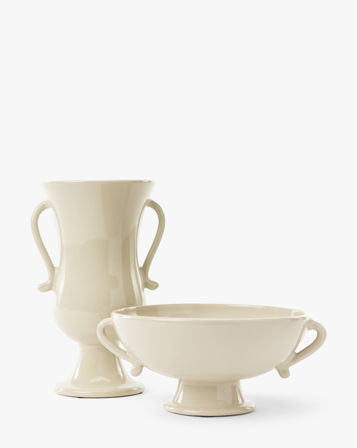 The Delphine Footed Bowl is a cream-colored ceramic vase with a glossy finish, side handles, and a pedestal base. Its bowl shape and elegant design make it perfect for displaying flowers or as a decorative accent by McGee & Co.