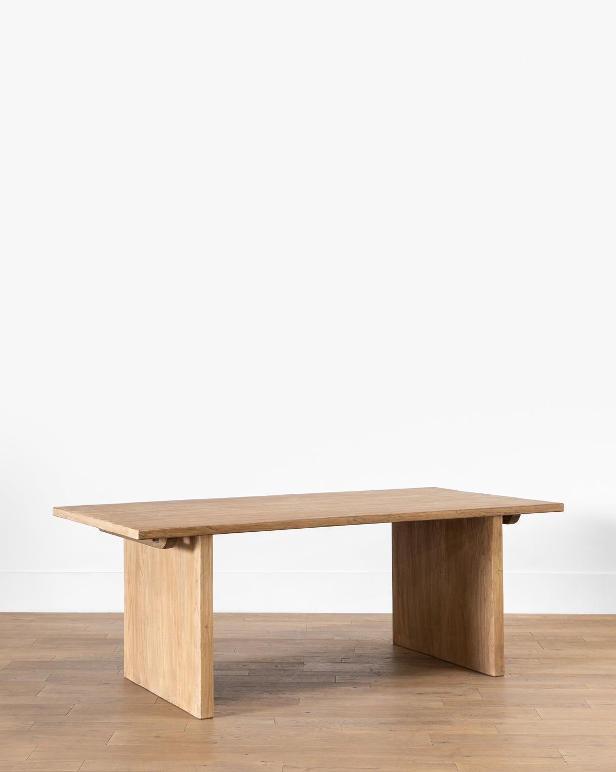The Dillon Extension Dining Table features a minimalist wooden design with a rectangular top and thick, flat legs, reminiscent of reclaimed elm, set on a light wood floor against a plain white wall by McGee & Co.