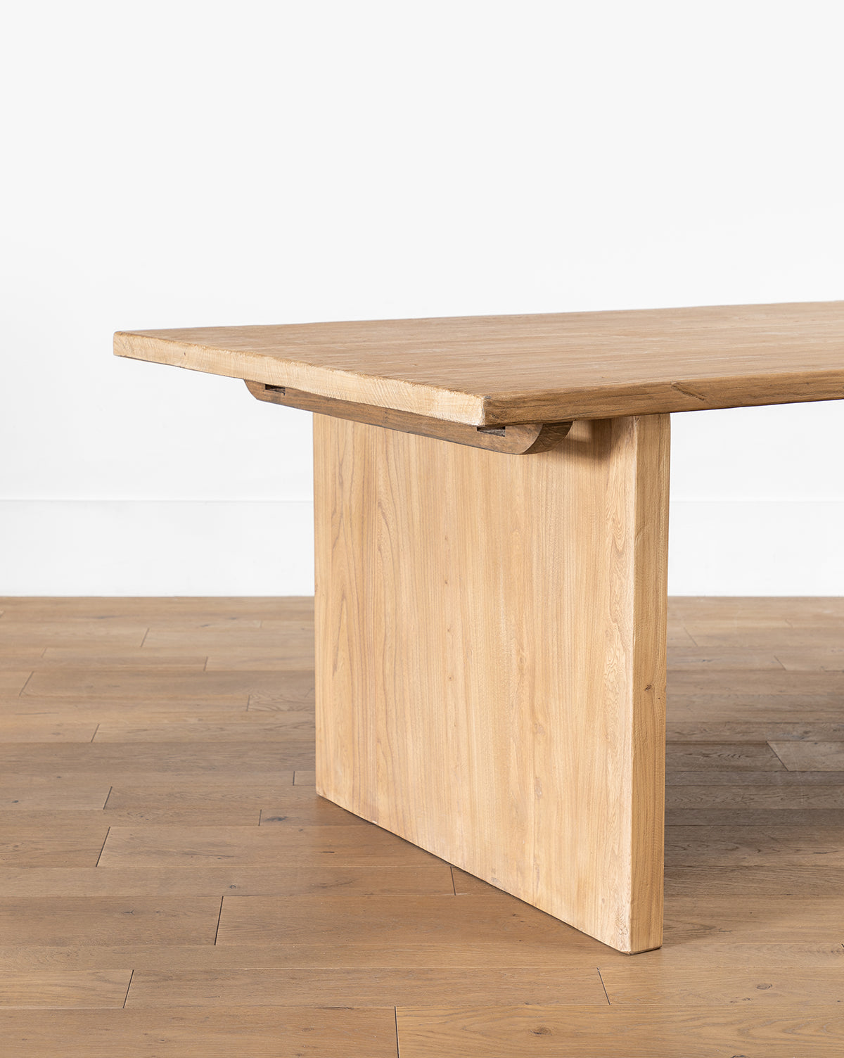 The Dillon Extension Dining Table features a thick rectangular top and wide, flat legs, creating a modern rustic look, shown on a wooden floor against a plain white wall by McGee & Co.