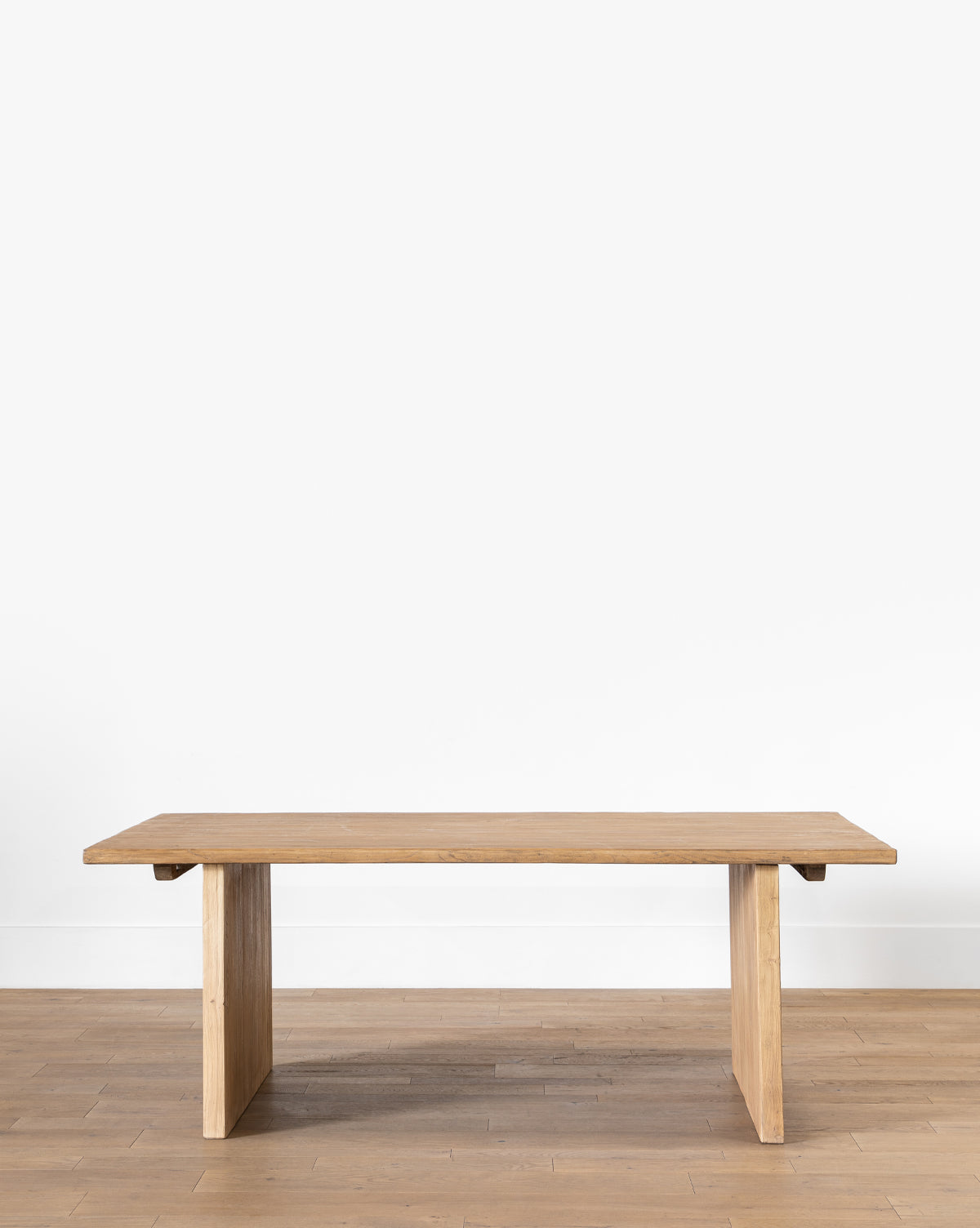 The Dillon Extension Dining Table features a minimalist reclaimed elm design with a rectangular top and two wide, flat legs, set on a light wood floor against a plain white wall, by McGee & Co.