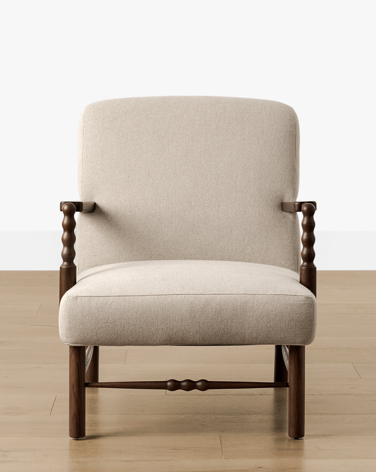 The Earnshaw Lounge Chair showcases neutral upholstery and an English oak carved wooden frame, set on a light wood floor with a plain white wall backdrop, by McGee & Co.