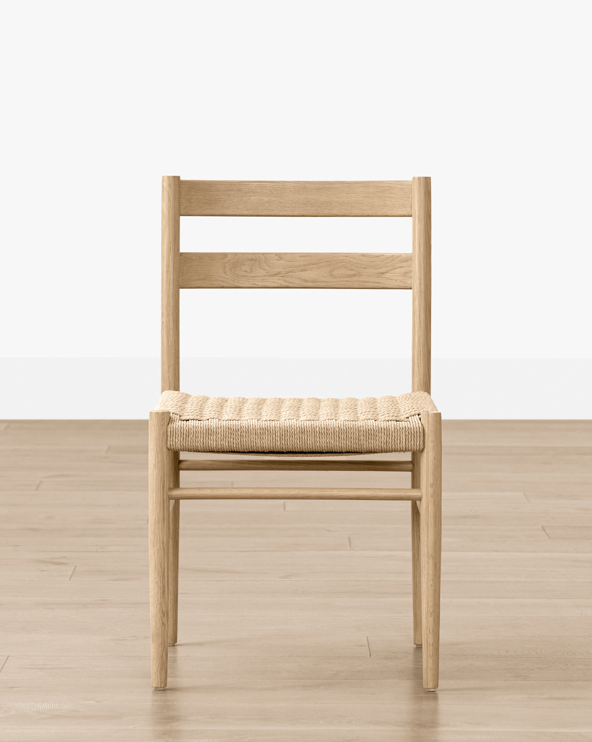 The Eloise Woven Chair features simple Danish design with a wooden frame, woven seat, and two horizontal slats on the backrest—ideal for any dining room, shown on a light wood floor against a plain white wall, by McGee & Co.