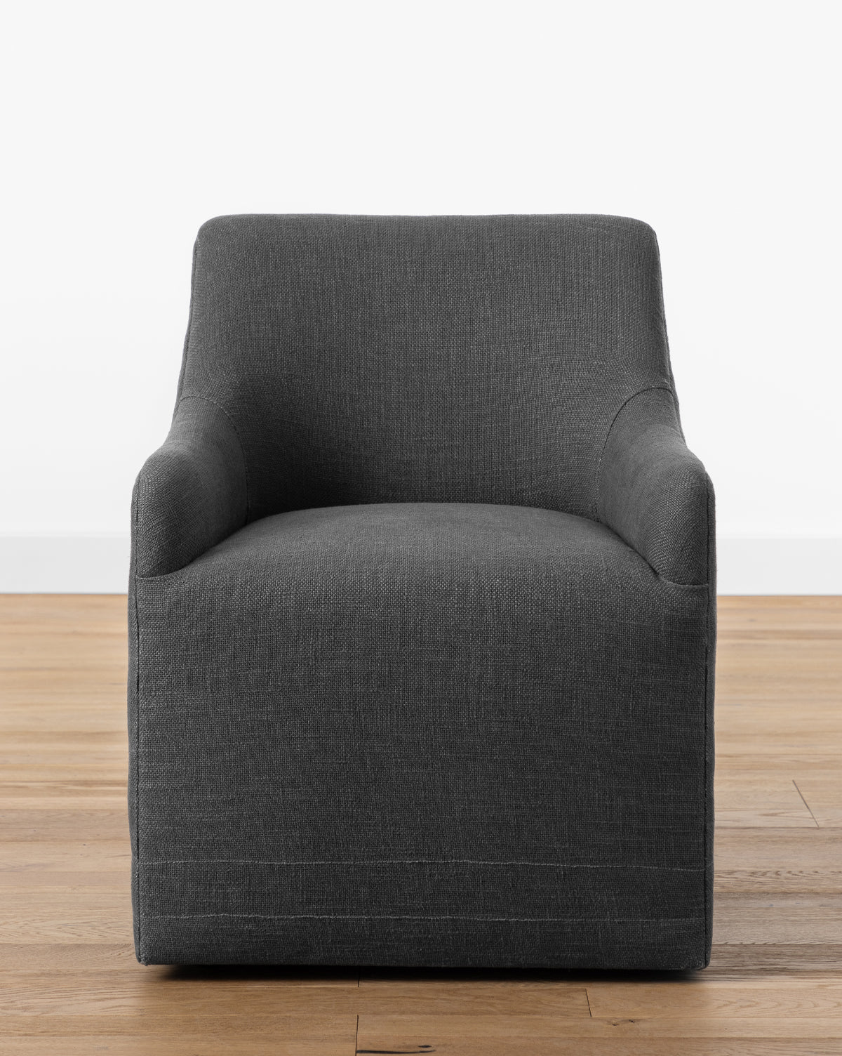 The Elton Office Chair features a modern boxy design with dark gray linen-blend upholstery, slightly rounded arms, and adds office elegance when placed on a light wooden floor against a plain white wall, by McGee & Co.