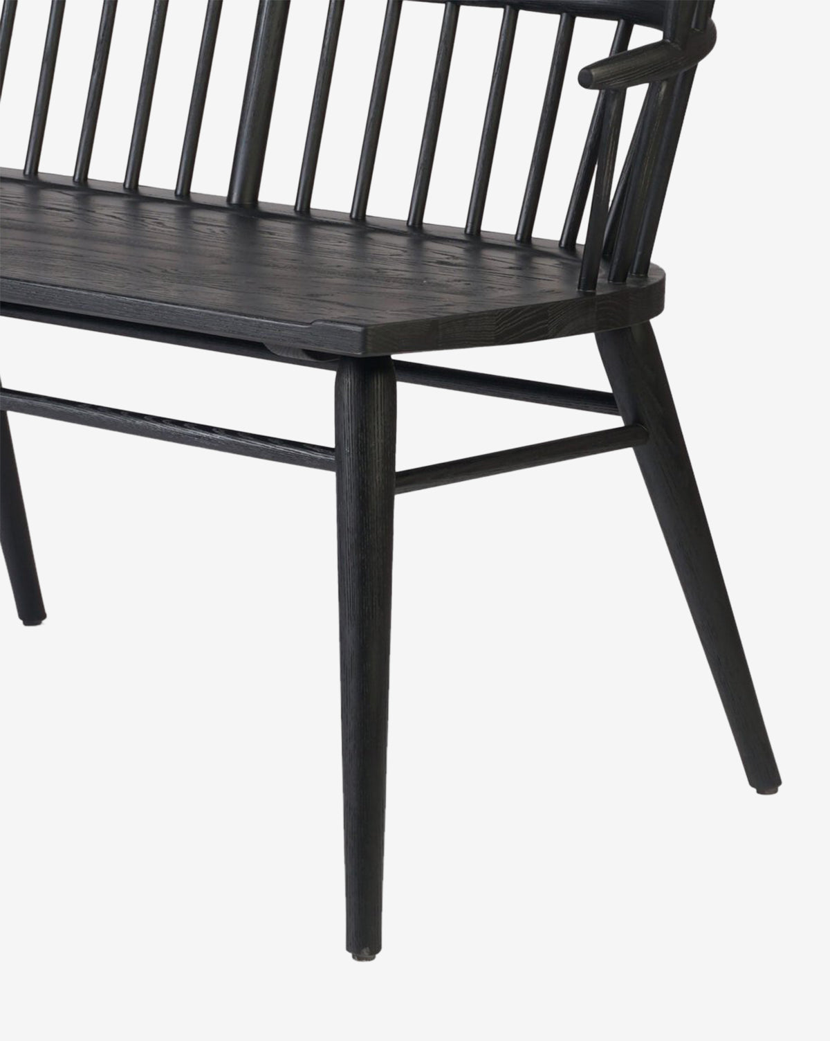 A close-up of the Elysia Bench, featuring angled legs, a flat seat, and vertical spindle backrest in solid ash. The image shows part of the modern bench against a white background, by McGee & Co.