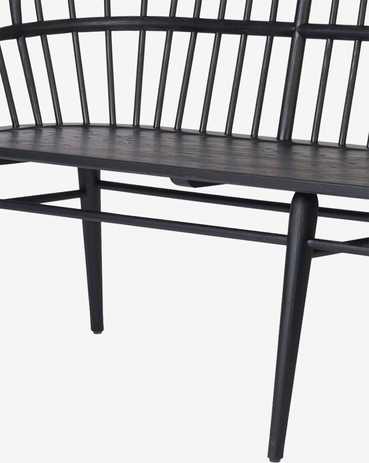 A close-up of the Elysia Bench, a modern seat with a black solid ash frame, spindle backrest, and tapered legs, set against a white background by McGee & Co.