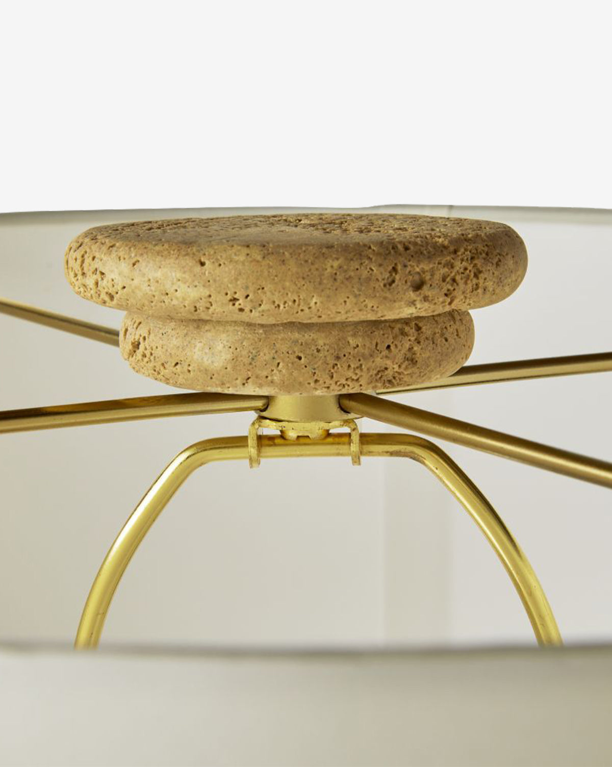 Close-up of the Eros Table Lamp’s interior, showcasing gold metal arms, a finial made of stacked textured beige stone discs, and an ivory microfiber shade for subtle elegance, by McGee & Co.