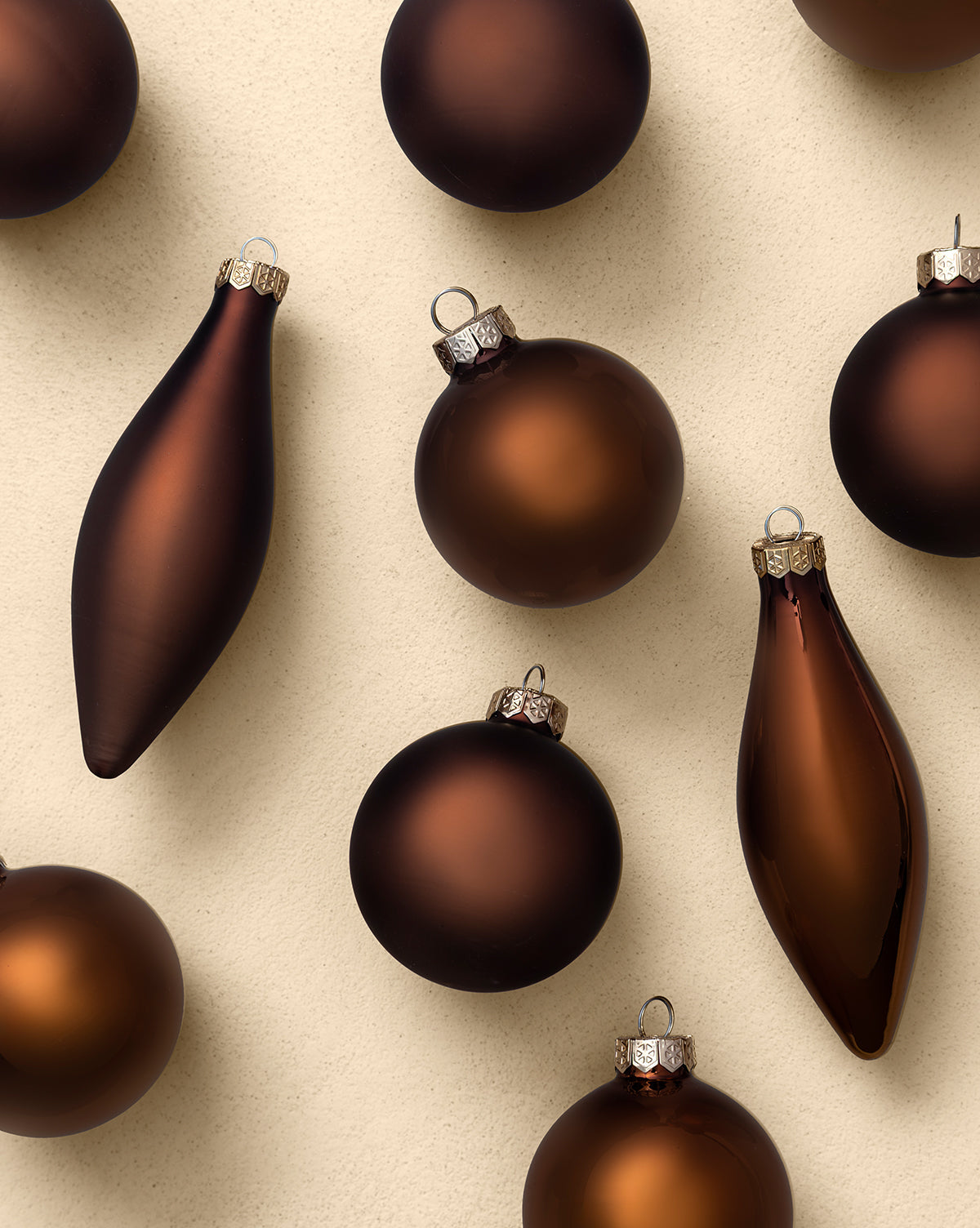 The Assorted Ornaments Espresso (Set of 10) features matte and glossy brown round and elongated ornaments, displayed on a light beige background—ideal for bringing modern sophistication to your holiday tree, by McGee & Co.