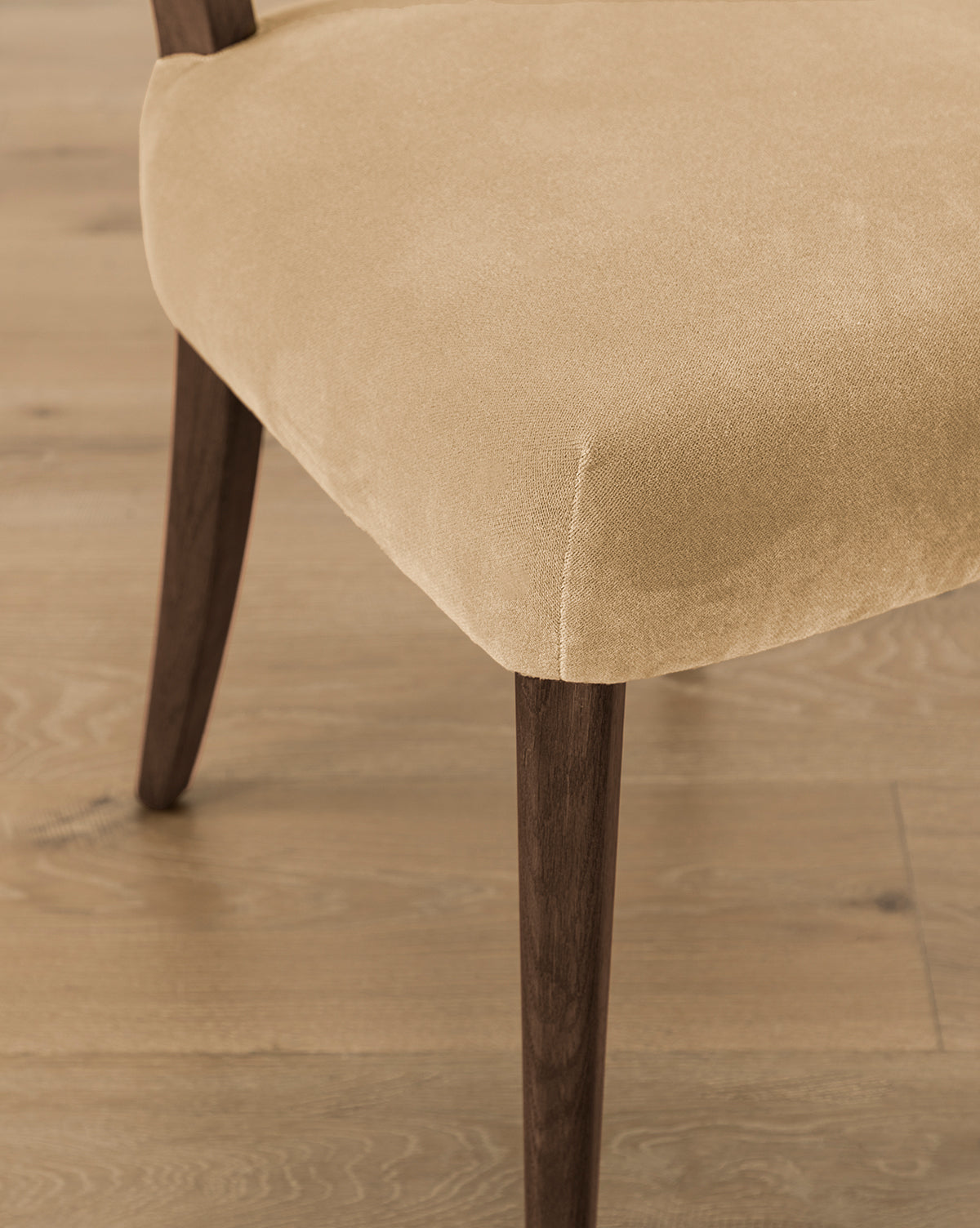 Close-up of the Etienne Dining Chair (Ready to Ship) featuring a light beige upholstered seat and dark wooden legs on a light wood floor, showcasing its elegant corner detail and vintage-inspired dining chair design, by McGee & Co.