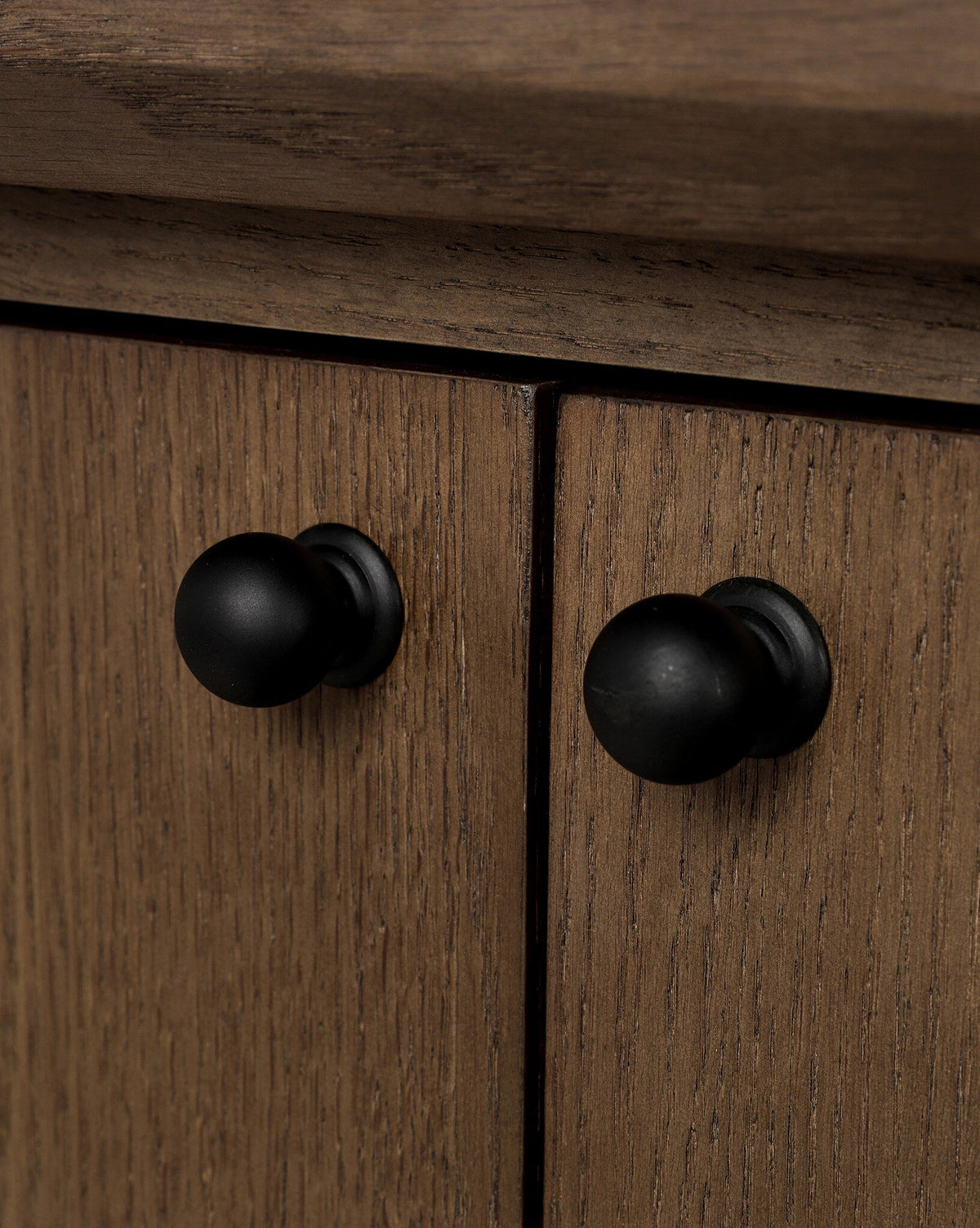 Close-up of two black iron hardware knobs on wooden cabinet doors with a natural brown grain, perfect for the Evaline Sideboard, by McGee & Co.