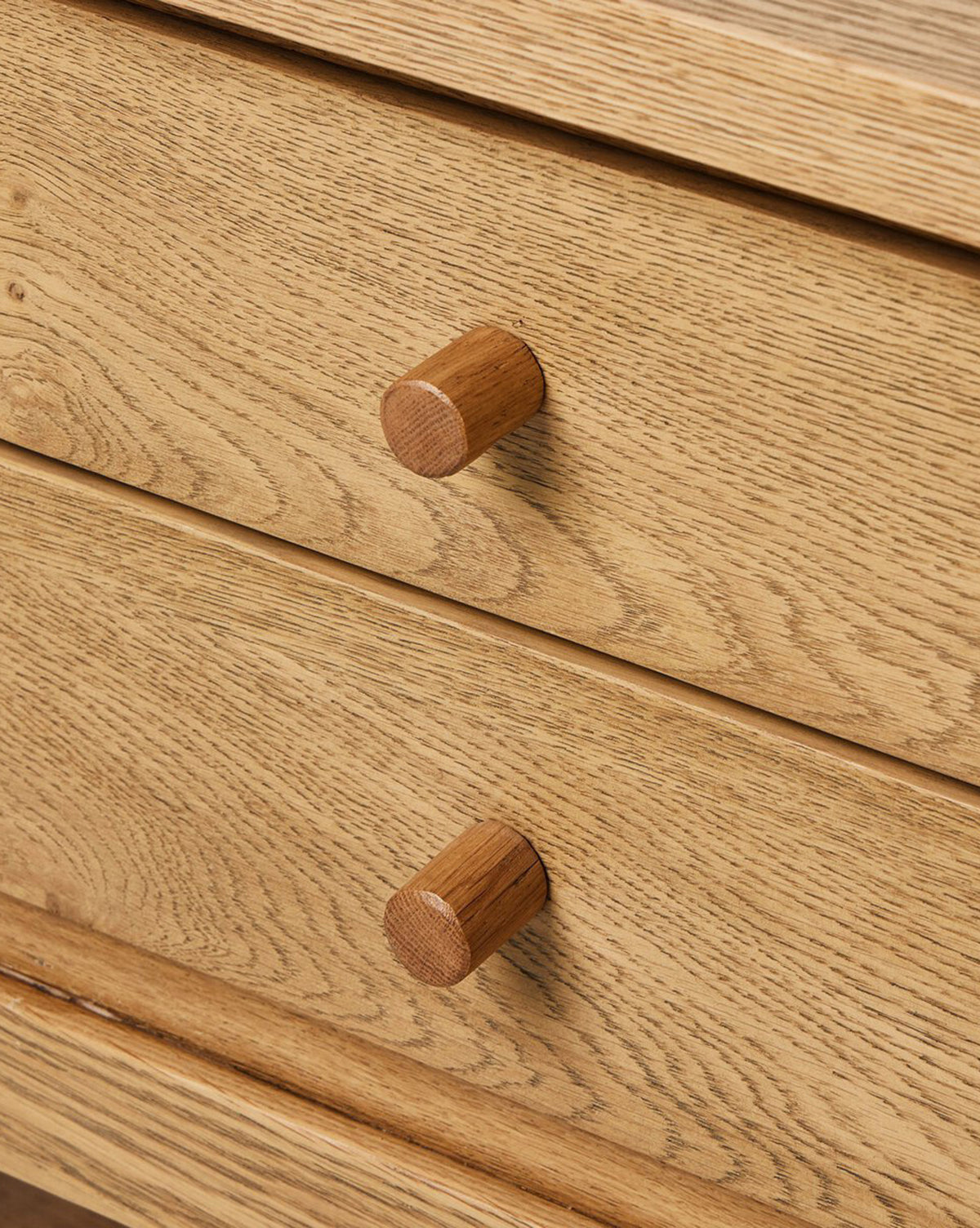 Close-up of two wooden drawers with round knobs highlights the natural wood grain and texture of the Faelan Nightstand in light oak veneer—perfect for modern bedrooms, by McGee & Co.