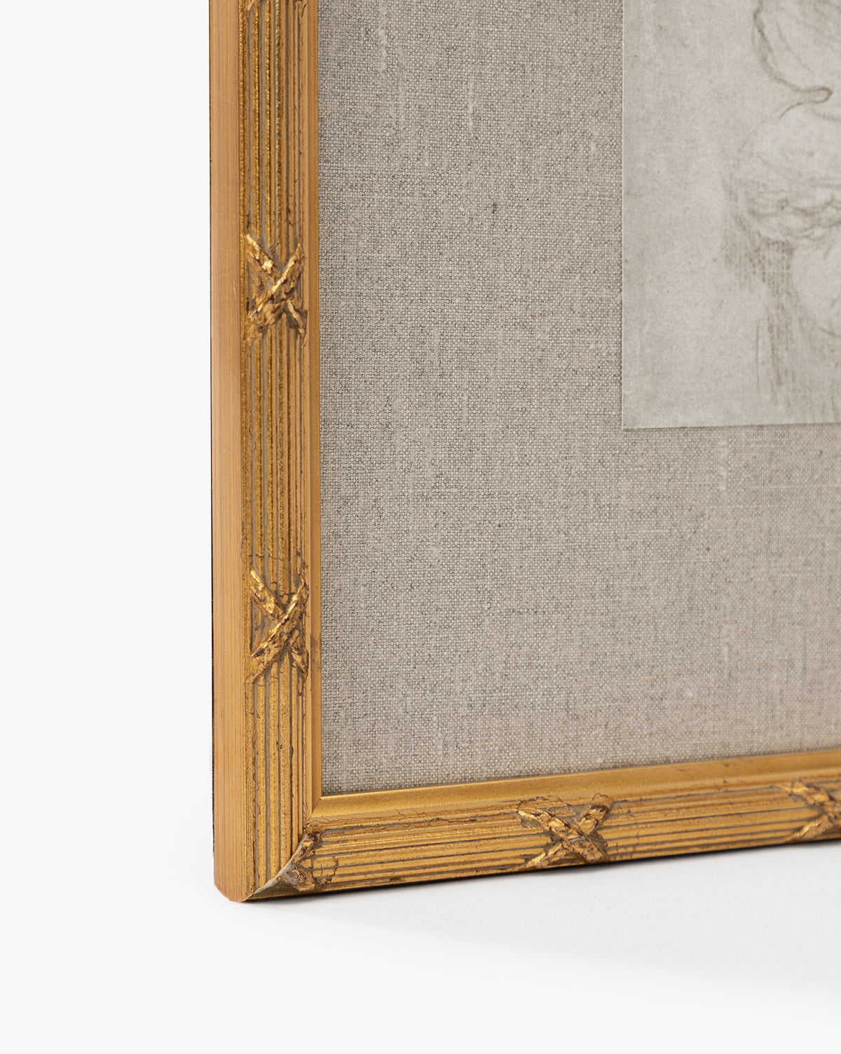 Close-up of the bottom left corner of a gold leaf frame with decorative detailing, holding a textured light fabric mat and a partially visible Feathery Floral giclée on paper by McGee & Co.