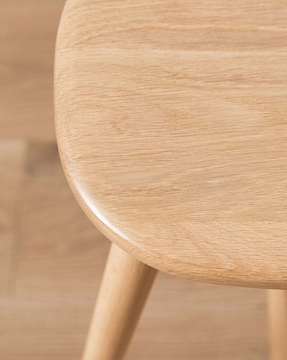 Close-up of the Fielder Counter Stools smooth, rounded seat and leg in a light oak finish, showcasing its natural wood grain, by McGee & Co.