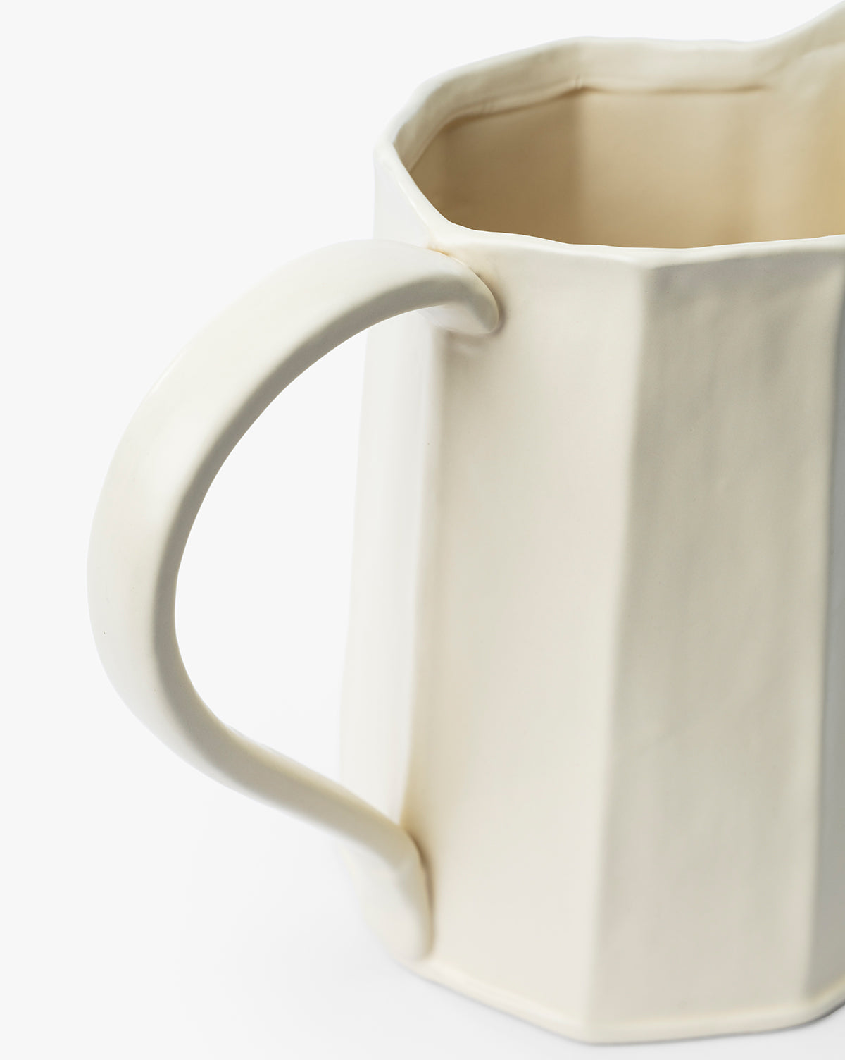 A close-up of the Fielding Ceramic Pitcher—cream-colored ceramic with a faceted geometric design and large curved handle—perfect for rustic kitchen decor, shown against a white background, by McGee & Co.