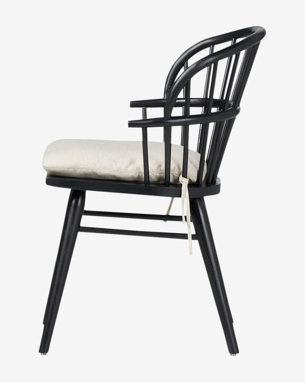 Side view of the Fiora Dining Chair, showcasing a curved backrest with spindles and a removable light beige seat cushion tied to its black wooden frame—ideal for complementing your dining table, by McGee & Co.