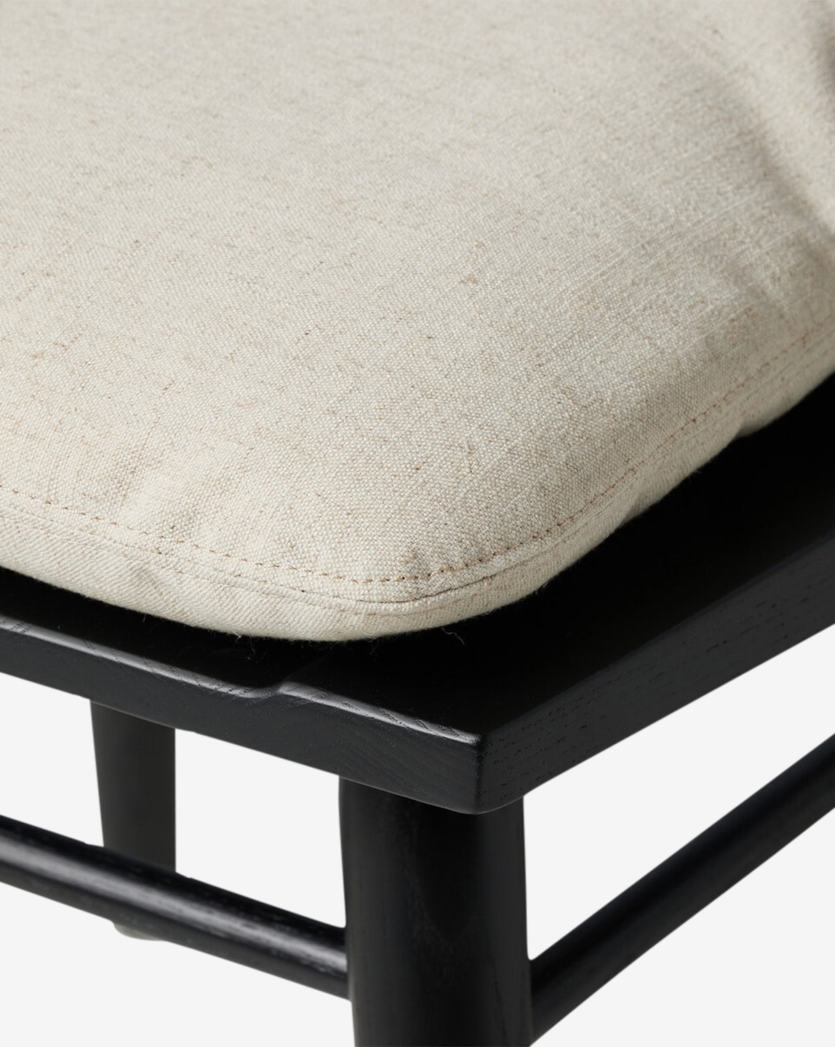 Close-up of a beige, textured removable seat cushion on the Fiora Dining Chair, a black wooden chair with visible stitching and a smooth, matte finish—ideal for any dining setup, by McGee & Co.