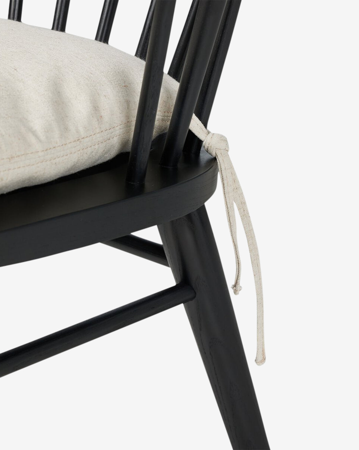 Close-up of the Fiora Dining Chair with a removable seat cushion attached to its black wooden frame, featuring a spindle backrest and angled legs, shown against a white background, by McGee & Co.