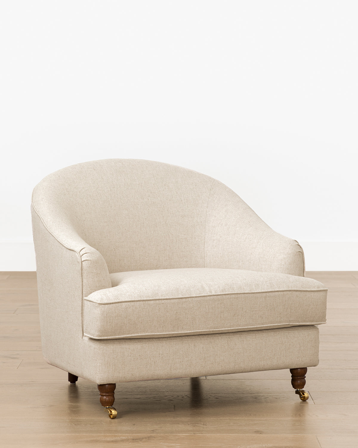 The Fletcher Lounge Chair (Ready to Ship) features beige upholstery, a rounded backrest, plush cushion, and wooden legs with brass casters—an inviting handcrafted lounge chair for any space, by McGee & Co.