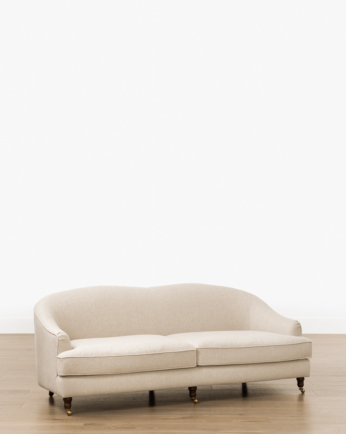 The Fletcher Sofa 76 (Ready to Ship) is a cream-colored, upholstered, handcrafted sofa with a curved backrest and wooden legs on casters, shown on a light wooden floor against a white background, by McGee & Co. Customizable fabrics available.