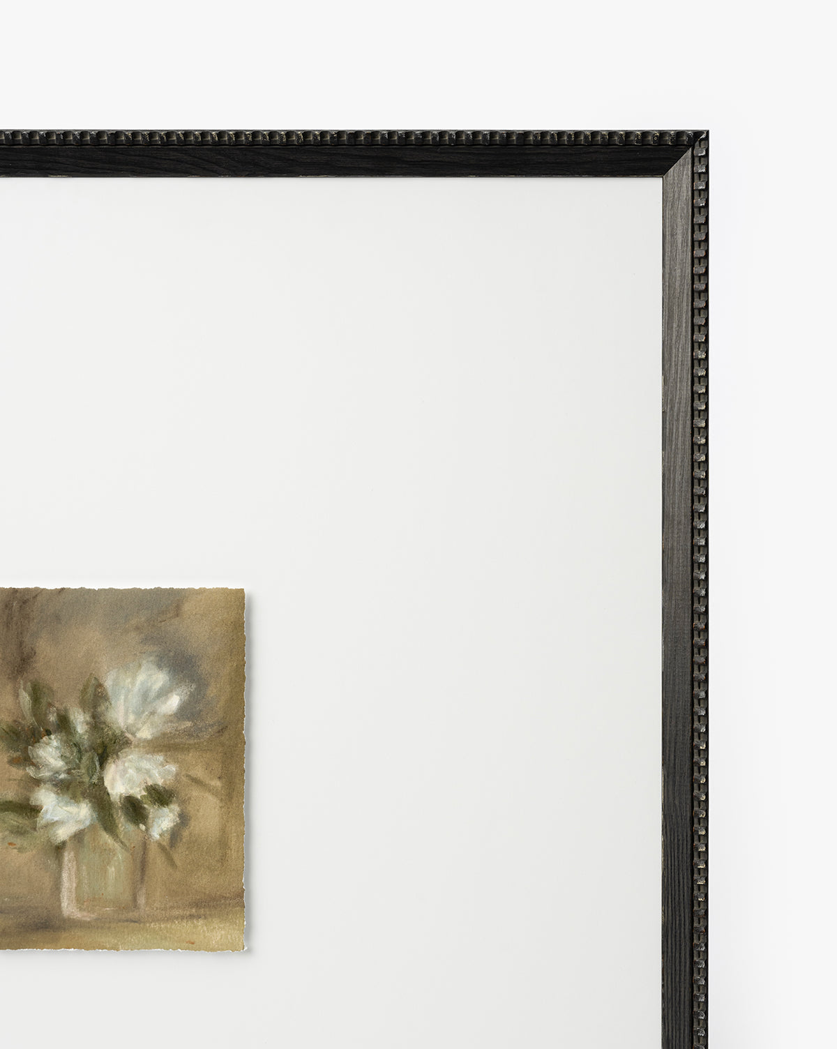 Flower Vase Still Life by Katie Mulder features white blooms in a small vase at the lower left of a large, mostly empty white canvas, all presented in a thin black textured frame, by McGee & Co.