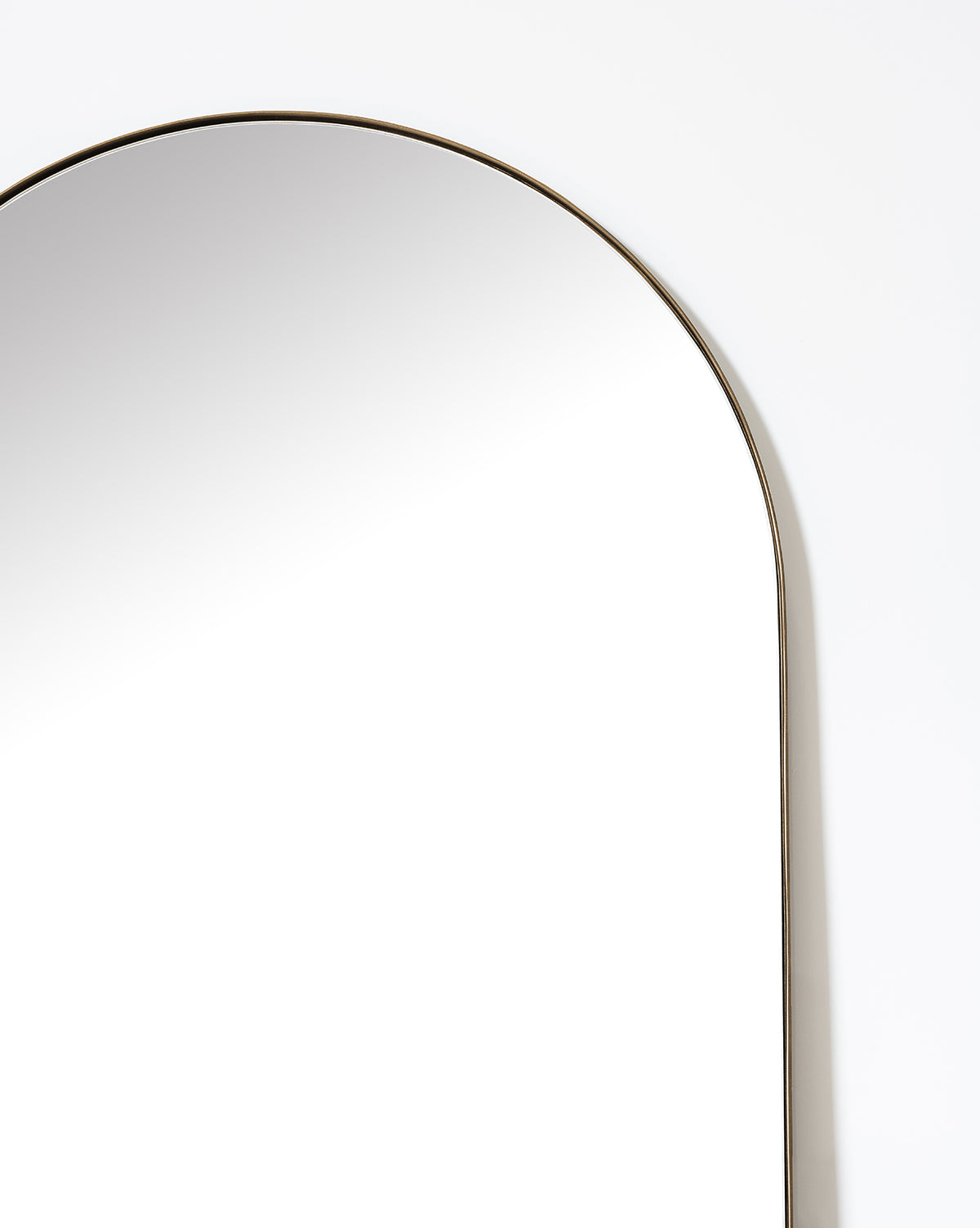 A close-up of the Gala Floor Mirror’s top, showcasing its slim metallic frame against a white wall—a stylish statement piece for any bedroom, by McGee & Co.