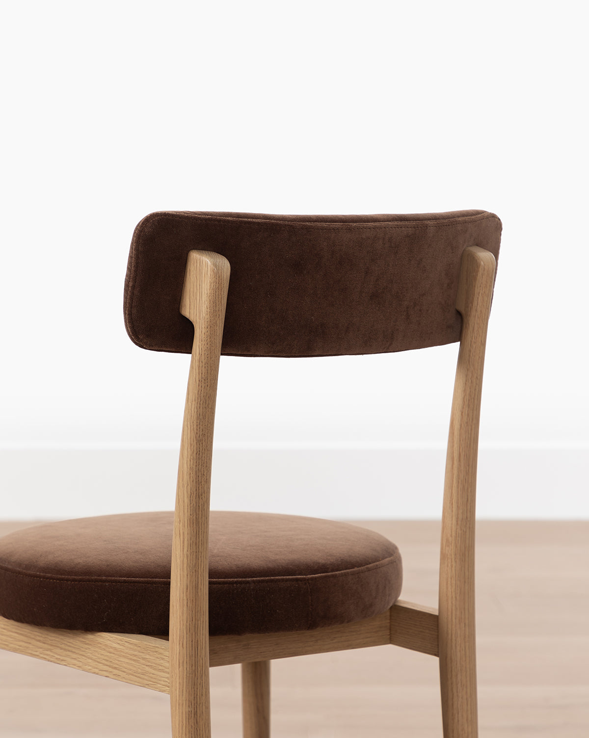 The Garance Dining Chair, featuring a white oak frame and a brown performance velvet cushioned seat and backrest, is pictured against a plain white background and light-colored floor by McGee & Co.