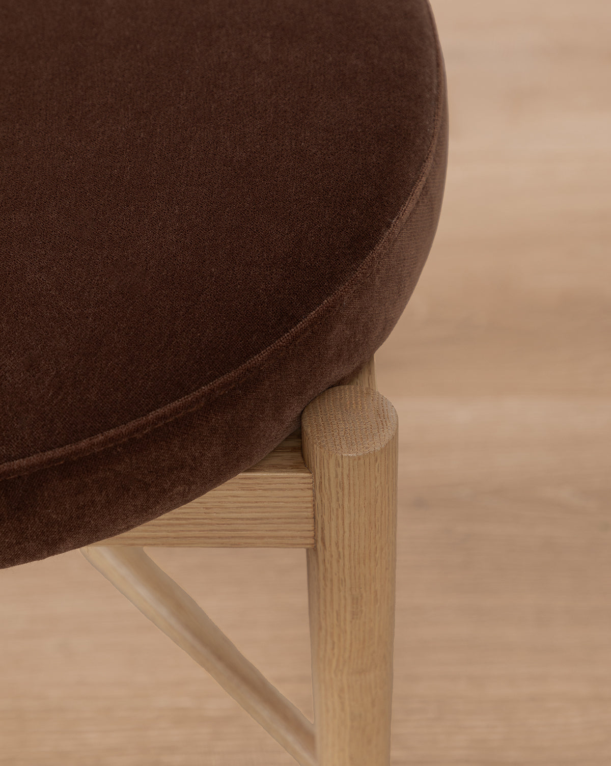 A close-up of the Garance Dining Chair, featuring a round dark brown performance velvet seat and light wood legs, set against a light wood floor by McGee & Co.