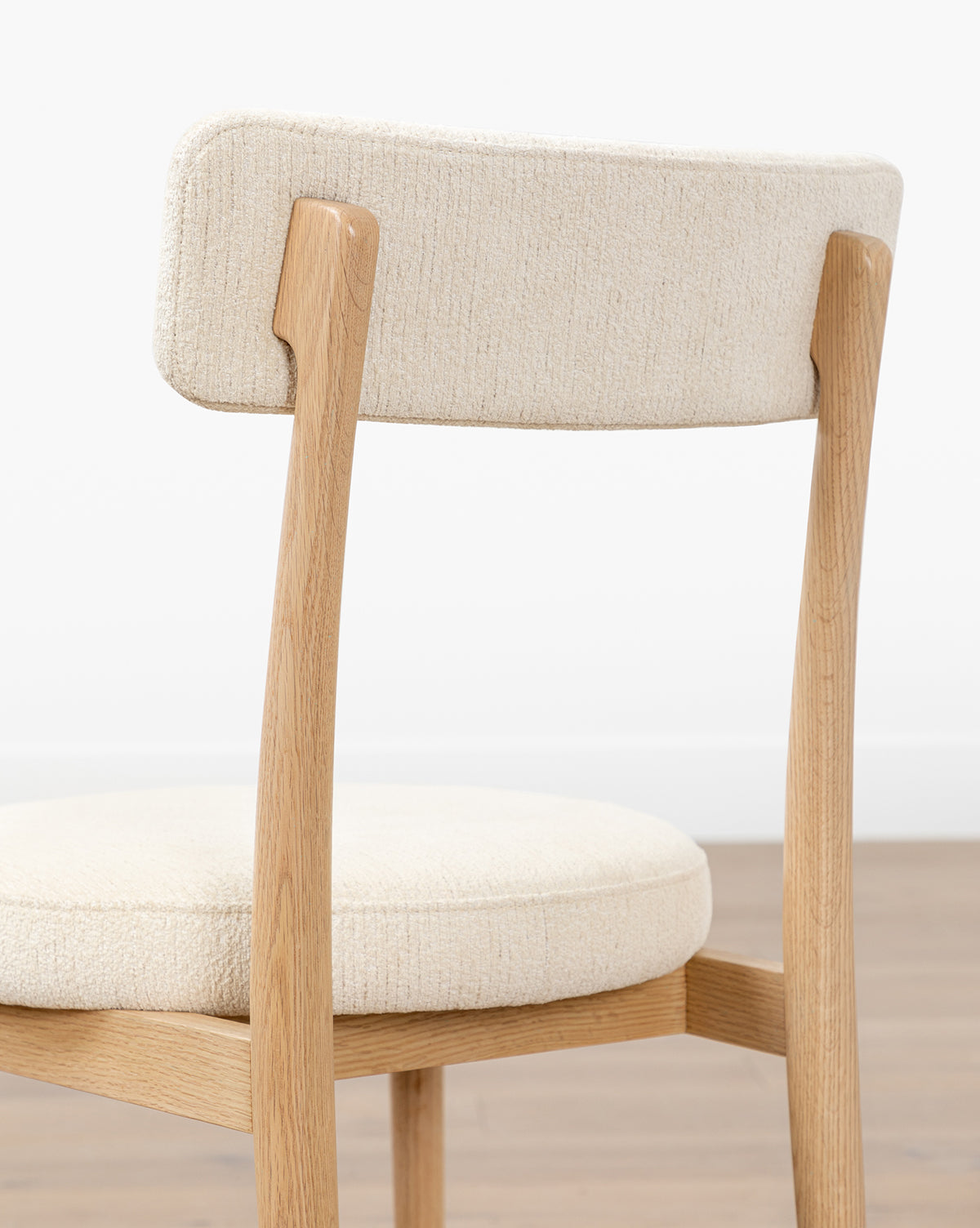 The Garance Dining Chair features a light performance velvet seat and curved backrest in white oak, shown from behind on a wooden floor against a plain white wall by McGee & Co.