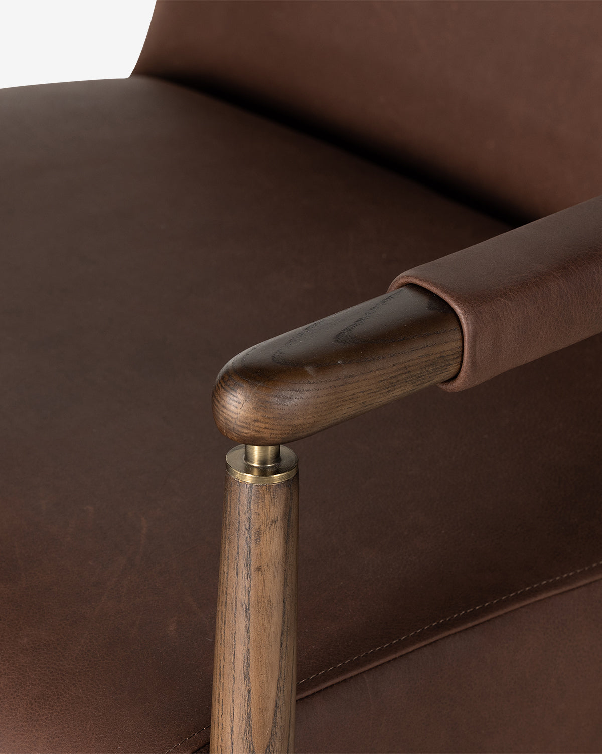 Close-up of the Gaston Lounge Chair, showcasing its top grain leather upholstery, solid ash frame, and brass detailing that highlight the leather’s rich texture and the smooth finish of wood and metal, by McGee & Co.