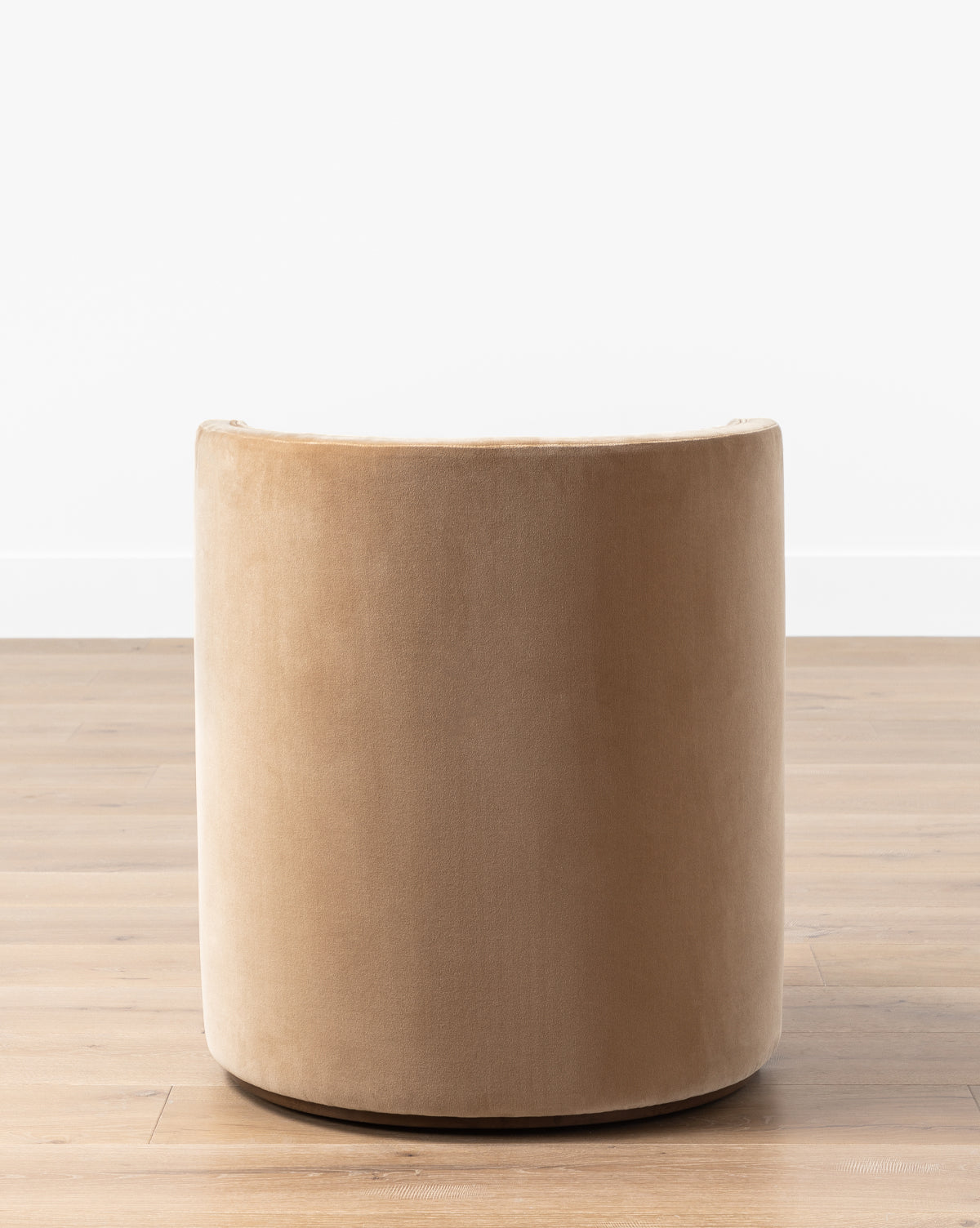 The Georgina Dining Chair (Ready to Ship) features a modern round barrel back in tan velvet, displayed on a light wooden floor against a white wall by McGee & Co.