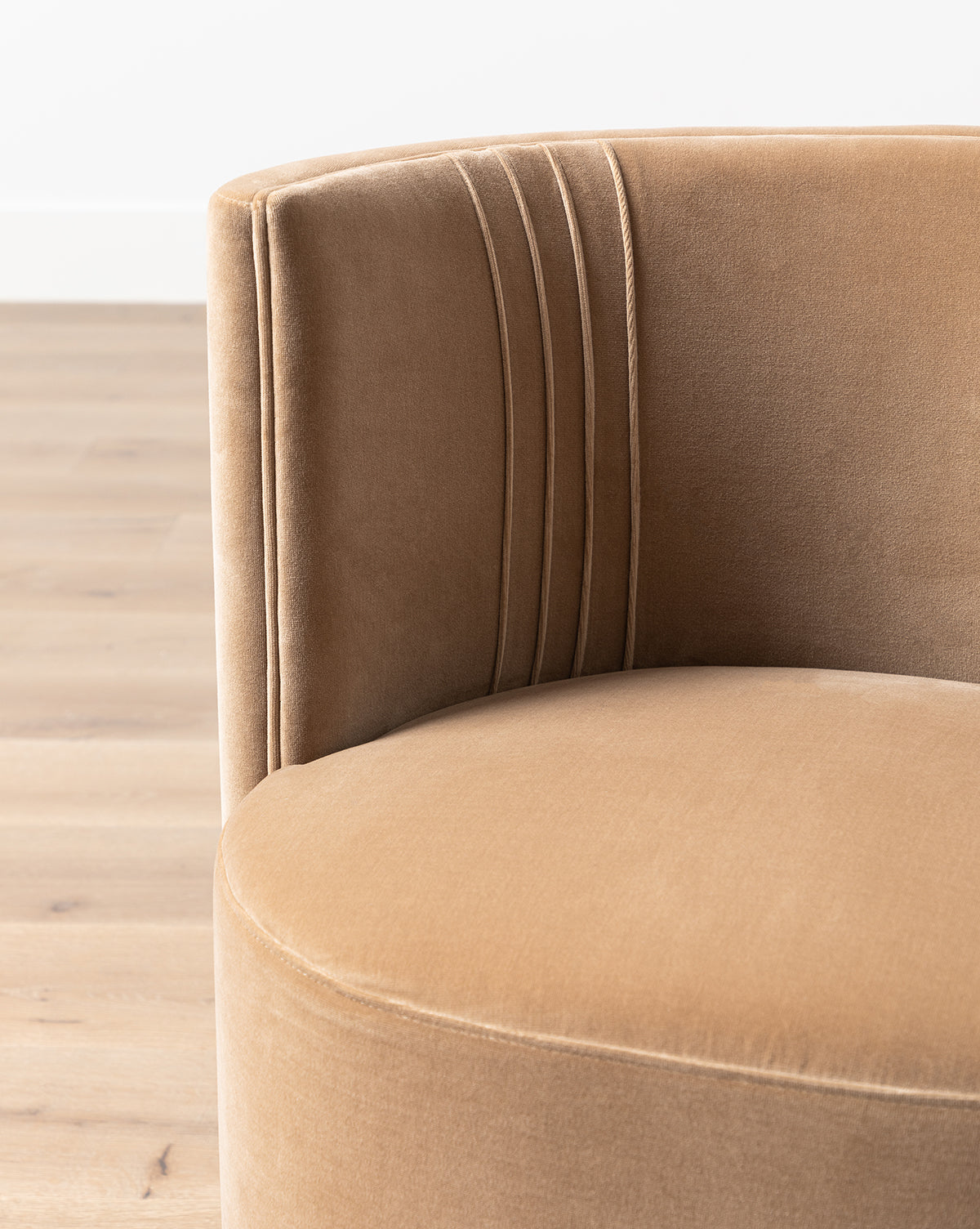 Close-up of the Georgina Dining Chair (Ready to Ship), featuring modern tan velvet upholstery, a barrel back, and vertical stitched detailing on the curved backrest, set on a light wood floor against a plain white wall, by McGee & Co.