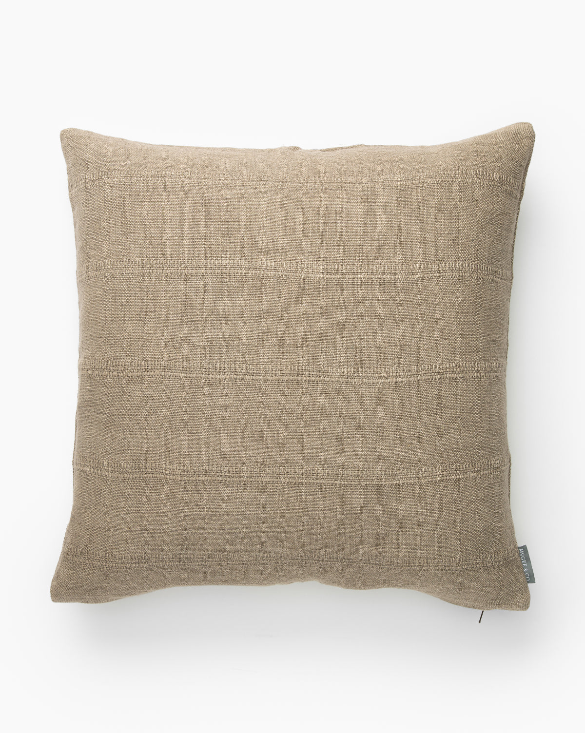 A square, light brown Gillespie Pillow Cover with subtle horizontal stitched lines is shown on a white background. A small fabric tag appears on the bottom right edge of this elegant linen cover, by McGee & Co.