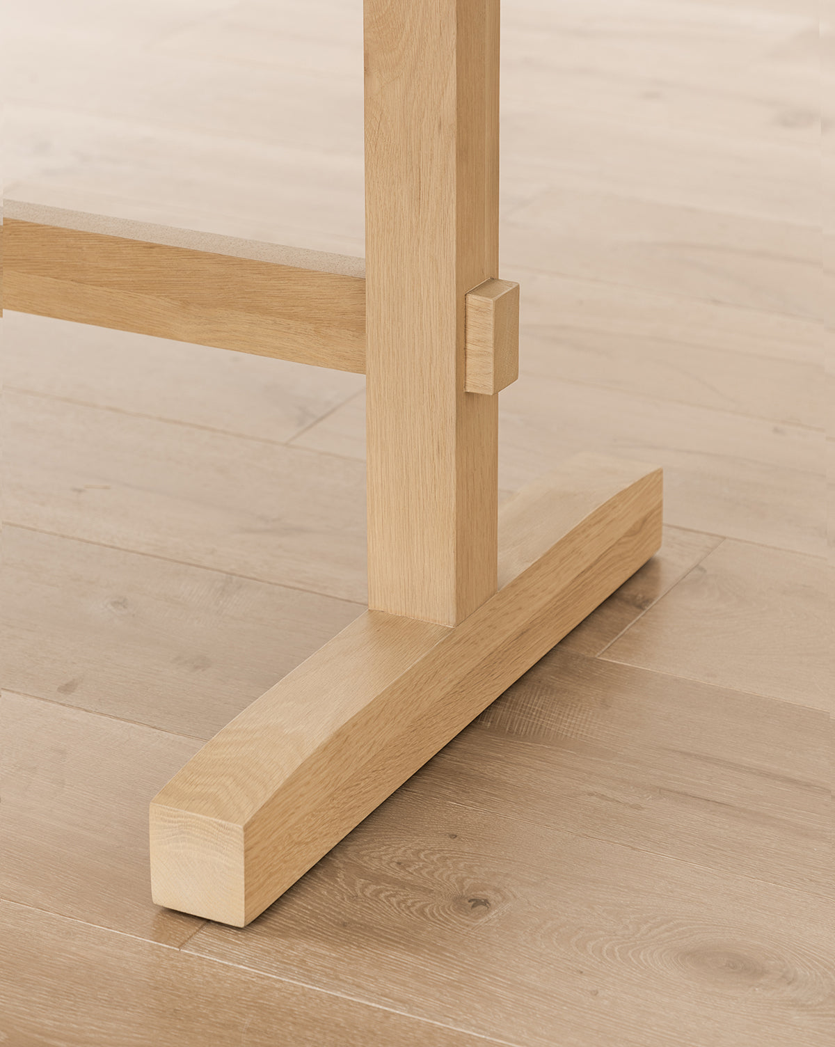 Close-up view of the Giselle Oval Dining Table’s white oak leg base on a matching light wooden floor, showcasing its clean lines and minimalist, sturdy construction, by McGee & Co.