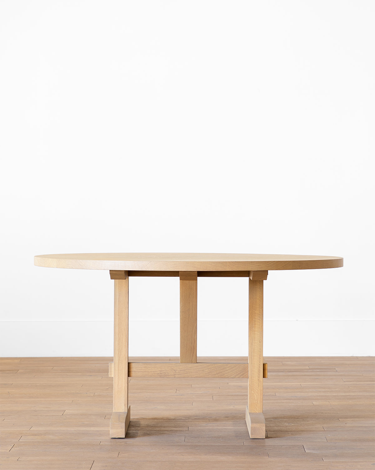 The Giselle Round Table, made from kiln-dried white oak with modern legs, stands on a wooden floor against a white wall by McGee & Co.