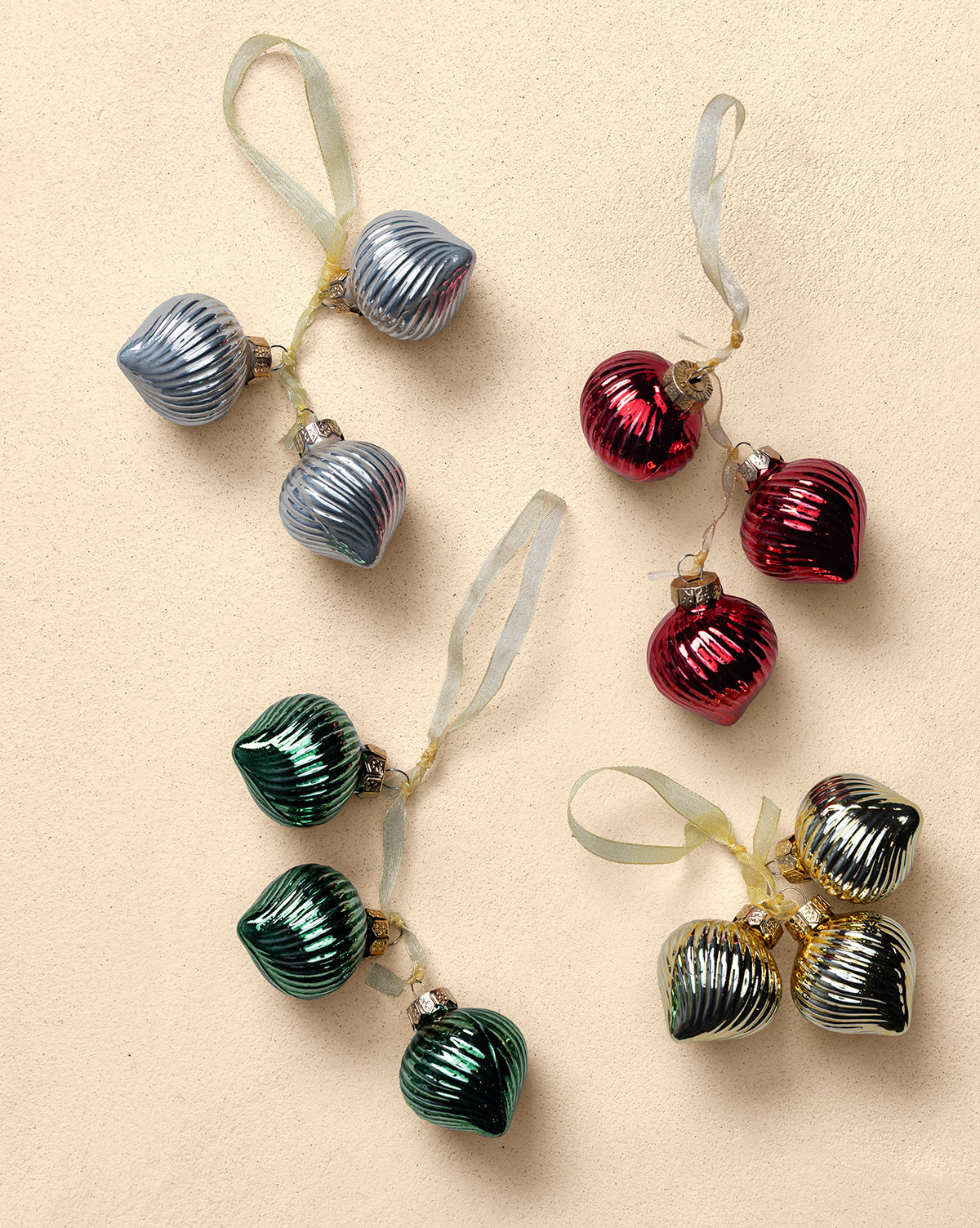 The Glass Bundle Ornaments (Set of 4) feature vintage-inspired silver, red, green, and gold ornaments, paired by color on a beige surface and tied with ribbon loops for festive holiday tree decor, by McGee & Co.