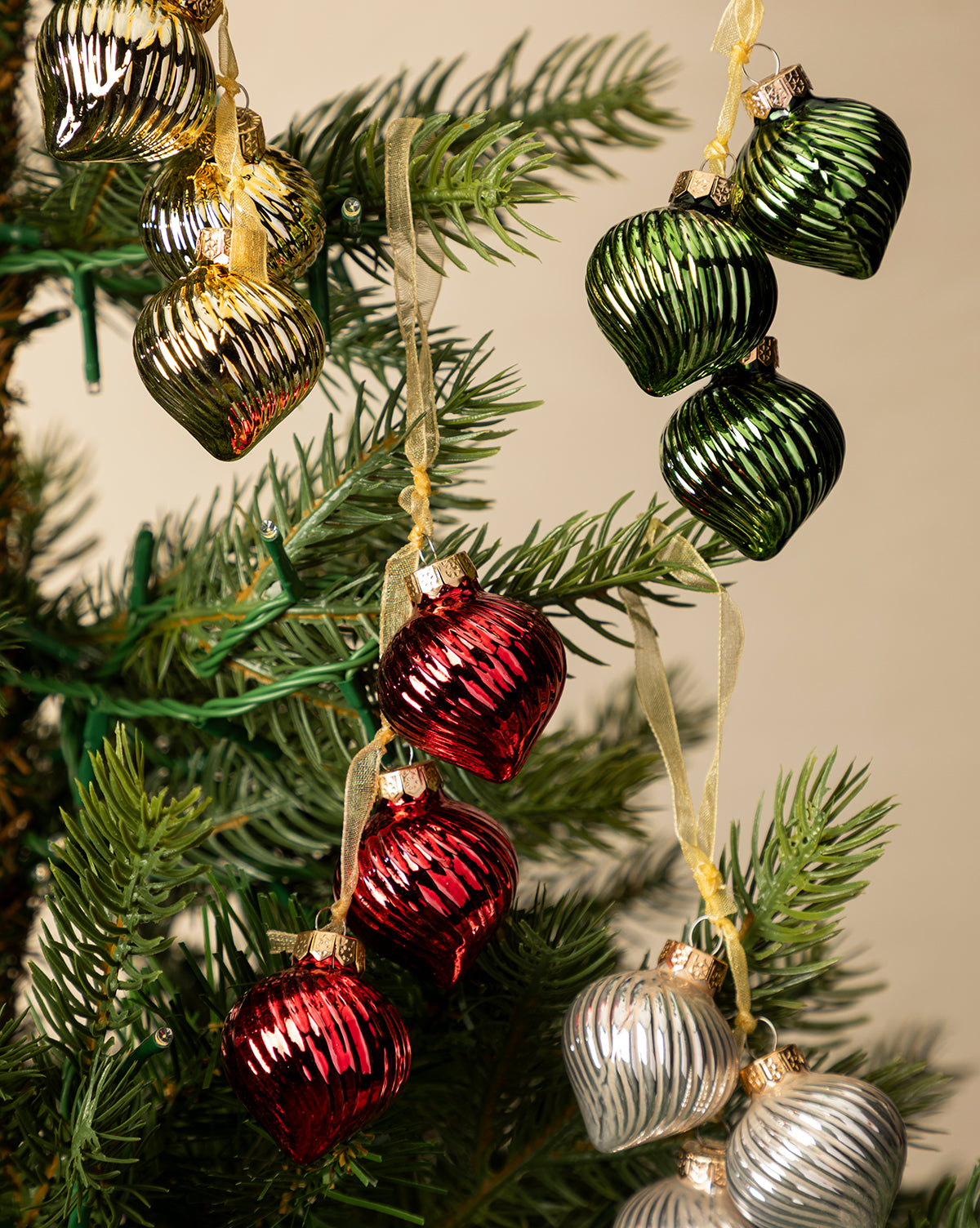 Close-up of a Christmas tree adorned with shiny gold, green, red, and silver ornaments from the Glass Bundle Ornaments (Set of 4), each hanging on gold ribbons amid festive holiday decor, by McGee & Co.