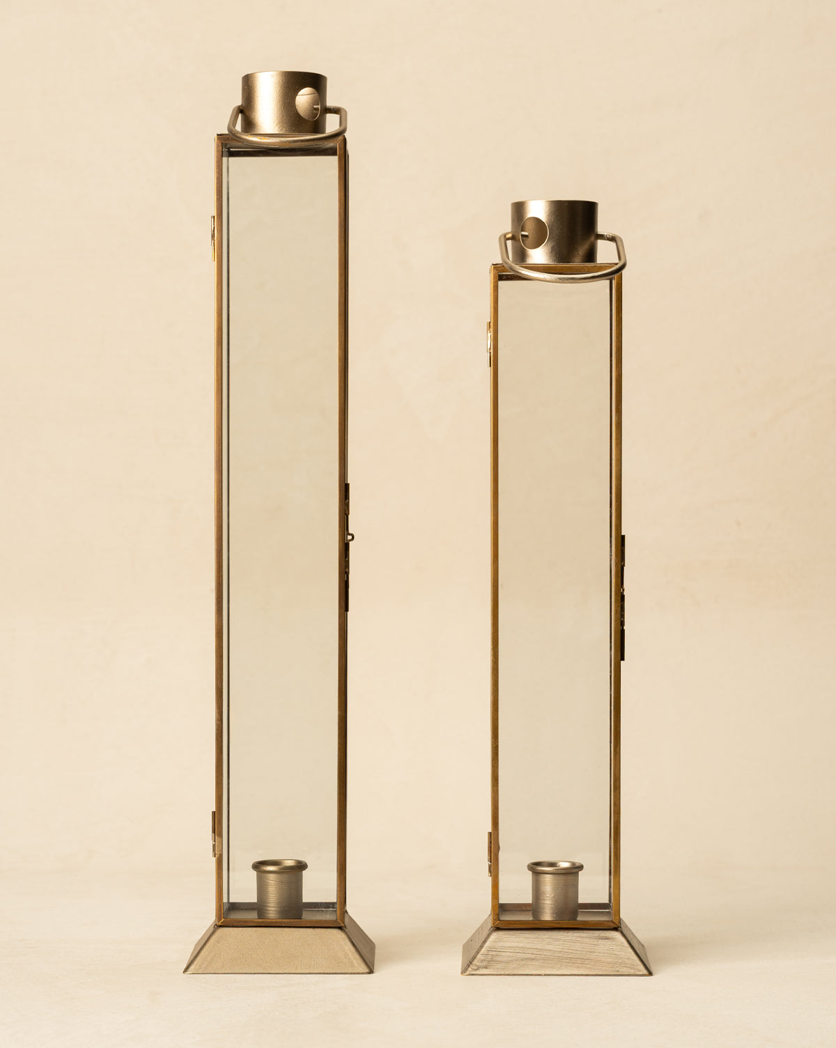 Two tall Glass & Metal Lantern Taper Holders with brass frames stand side by side on a neutral background. Each lantern has a top handle and an interior candle holder, adding stylish illumination to your space, by McGee & Co.