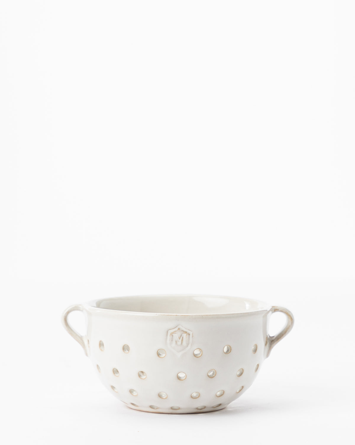 The Glazed Berry Colander is a white ceramic bowl with two handles and small round holes, ideal for stylish kitchen decor, shown on a plain white background, by McGee & Co.