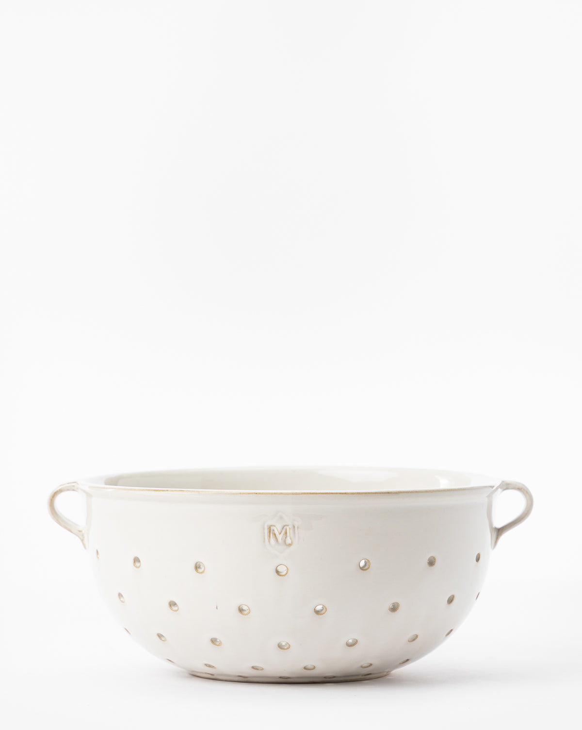 The Glazed Colander, featuring white ceramic, small round holes, dual side handles, and an embossed “M” on the front, adds a stylish touch to your kitchen or serveware collection. Shown against a plain white background by McGee & Co.