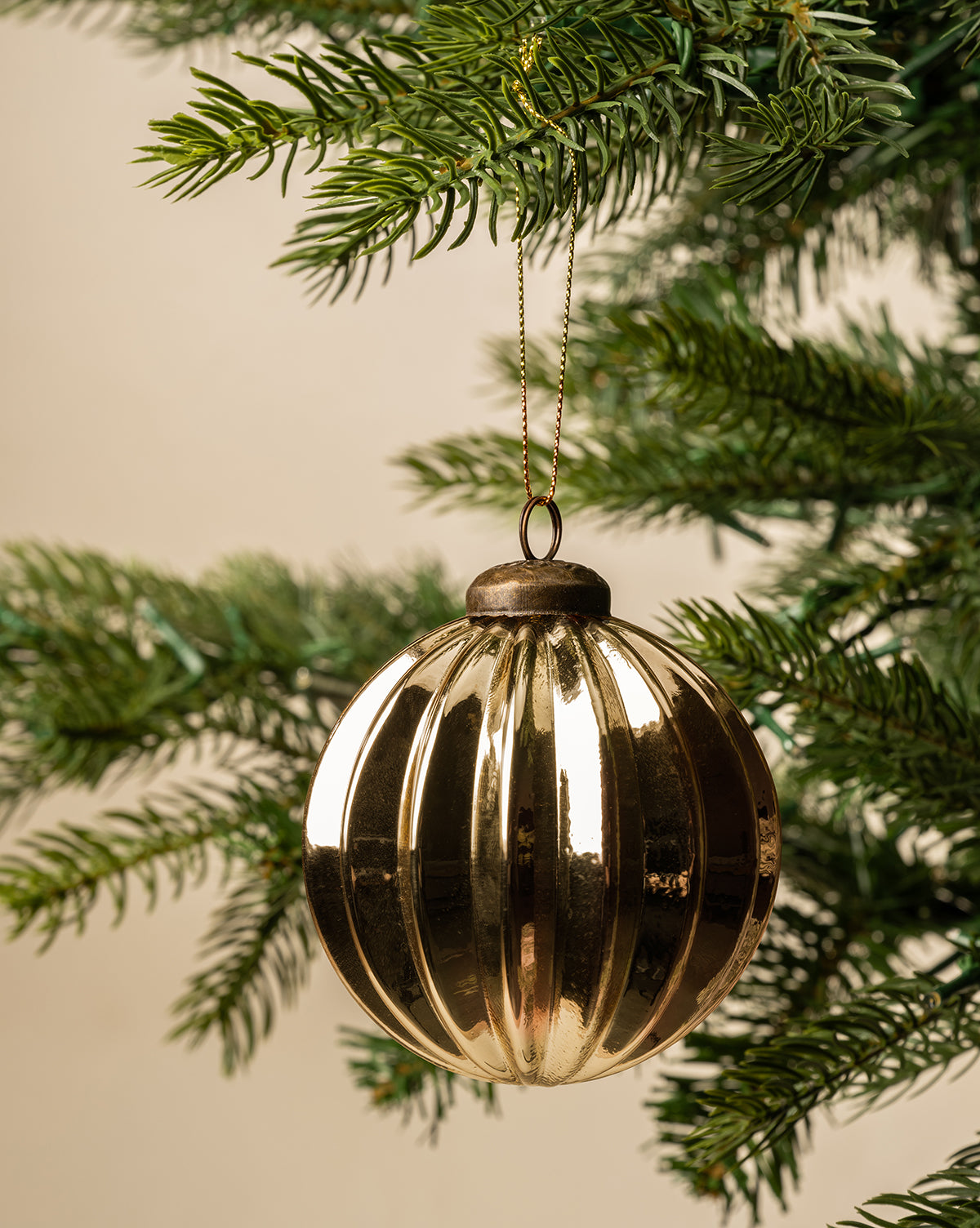 A 3" Gold Bauble with a shiny finish hangs from the branch of a green Christmas tree against a neutral background, by McGee & Co.
