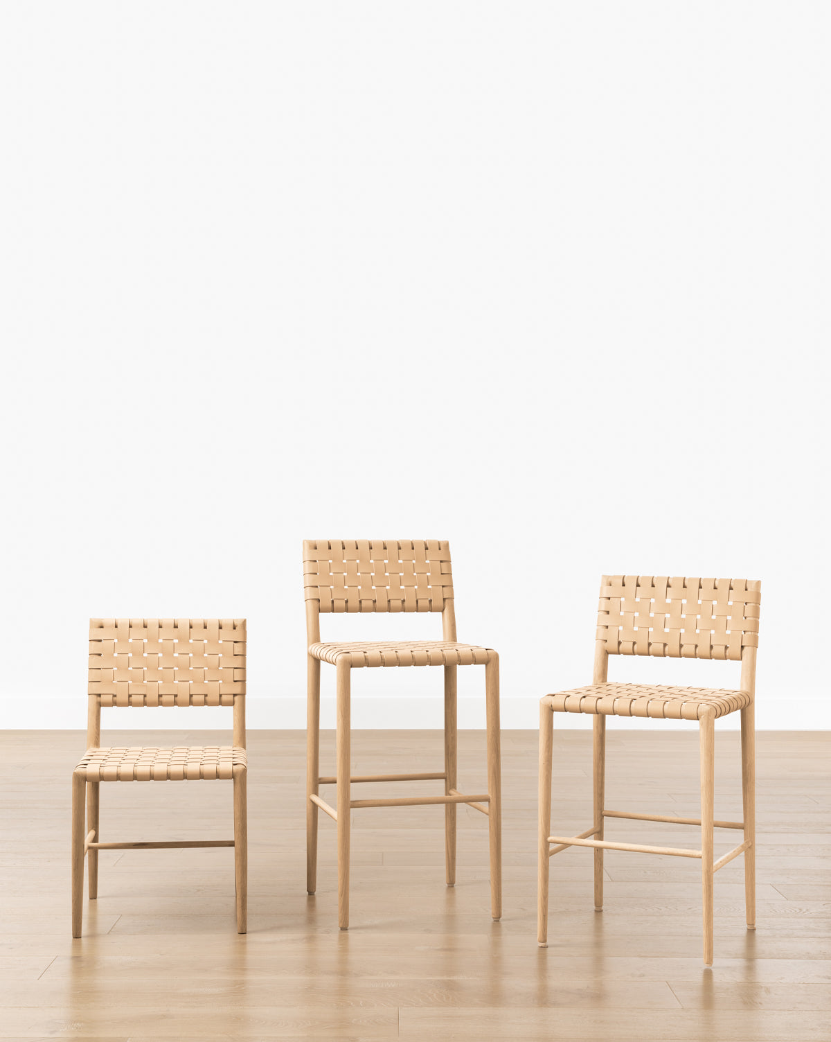 Three Greely Stools with white oak frames and woven seats are arranged in a row on a wooden floor against a plain white background, with their varying heights creating an appealing progression, by McGee & Co.