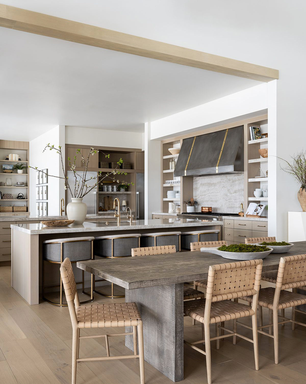 Modern kitchen with light wood cabinetry, large island with bar stools, open shelves, and a rustic dining table paired with Greely Dining Chairs in aniline dyed leather. Neutral tones and minimalist decor create an airy vibe, by McGee & Co.