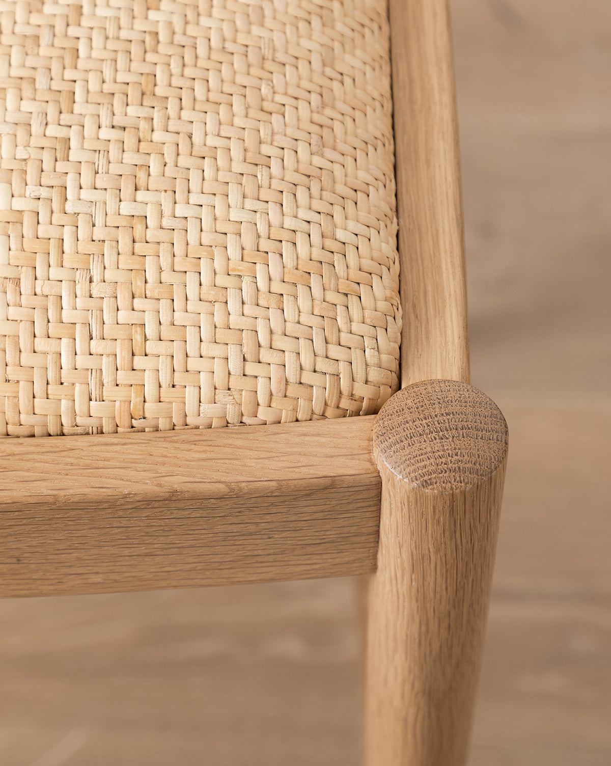 Close-up of the Hadden Natural Dining Chair’s oak corner with a woven rattan seat, highlighting the texture and craftsmanship of its materials on a light wood floor, by McGee & Co.