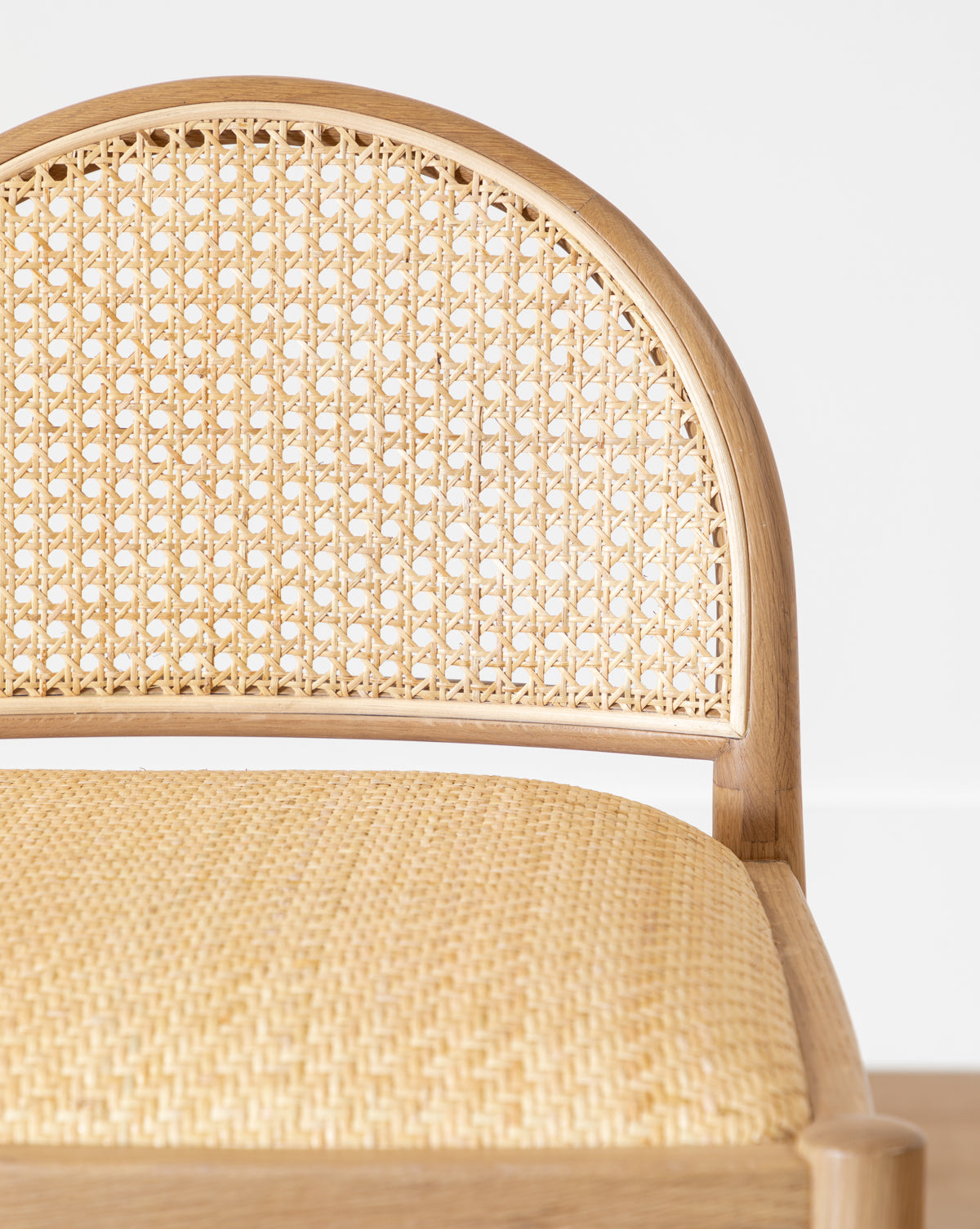 Close-up of the Hadden Natural Counter Stool, featuring a rounded woven cane backrest and matching light seat, set in an oak frame that reflects the relaxed elegance of coastal design, shown against a plain white background by McGee & Co.